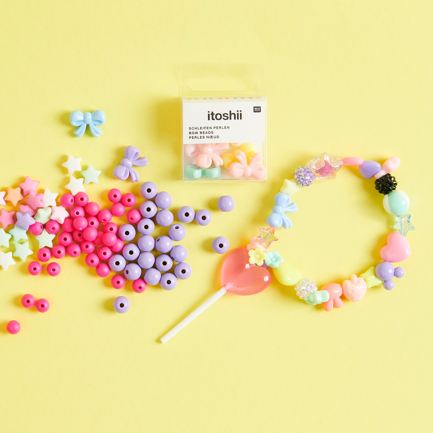 Itoshii Kunststoffperlen und Lolli-Anhänger in Pastellfarben auf gelbem Hintergrund, ideal für kreative Bastelprojekte.
