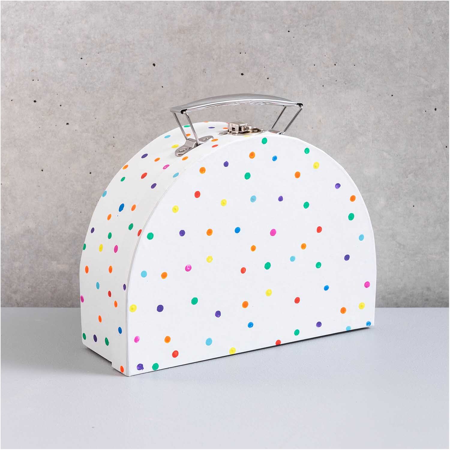 Koffer aus Pappe halbrund weiß mit bunten Punkten, von Rico Design, auf grauem Hintergrund.