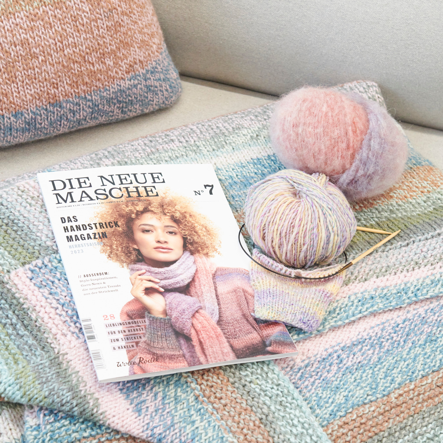 Die Neue Masche Nr. 07 Herbst zeigt ein Strickmagazin mit Wolle in Pastelltönen auf gestricktem Stoff.