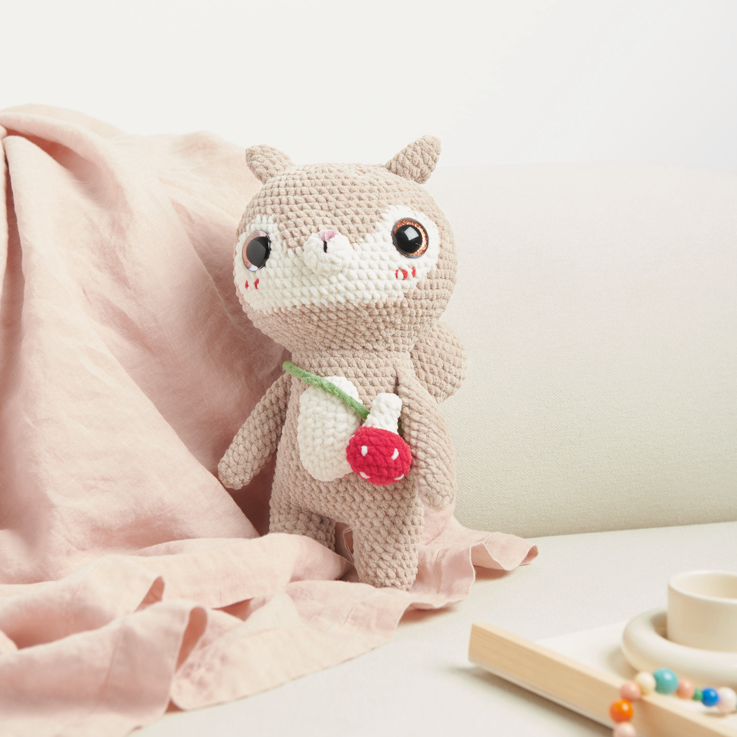 Häkelset Little Squirrel Modell 02: Ein niedliches, gehäkeltes Eichhörnchen mit rotem Accessoire auf einem Sofa.