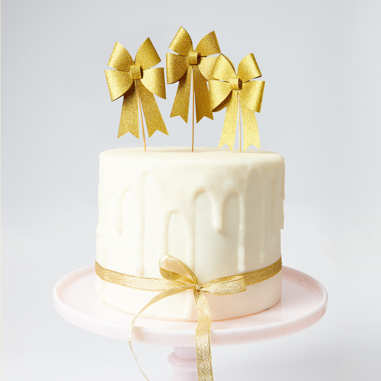 Picker Schleife Gold: Elegante goldene Schleifen von Rico Design auf einer weißen Torte als Dekoration.