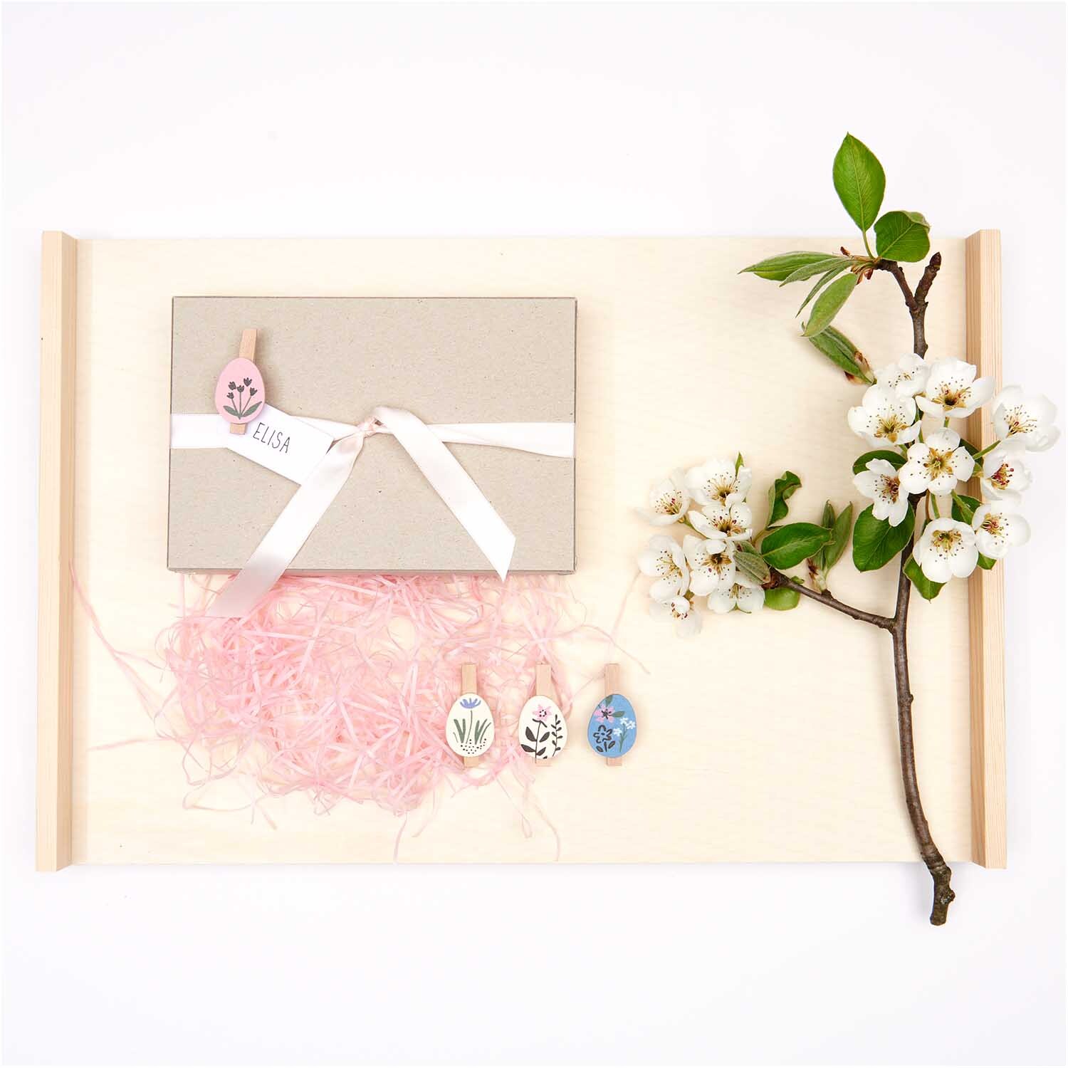 Ostergras 30g: Rosa Deko mit Geschenkbox, Schleife und blühendem Zweig auf hellem Hintergrund.