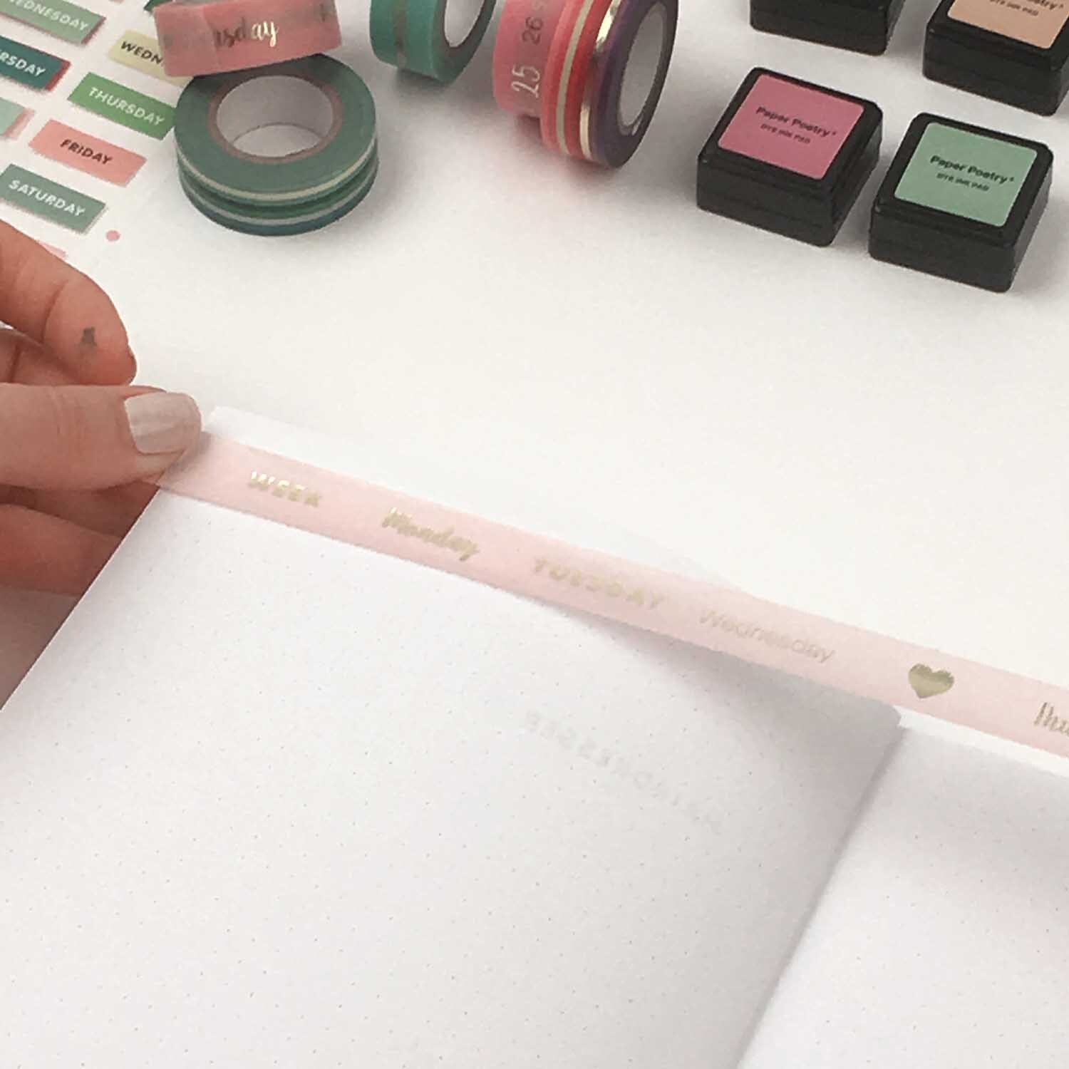 DIY Set Bullet Journal: Eine Hand dekoriert ein Notizbuch mit buntem Washi-Tape und Stempeln.