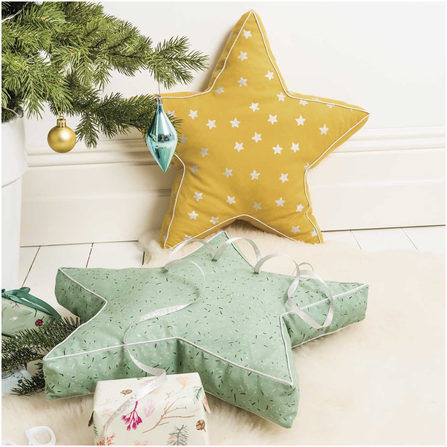 Druckstoff Nostalgic Christmas Streifen grün-metallic 140cm: Zwei sternförmige Kissen, eines in Gelb mit weißen Sternen, das andere in Grün, unter einem Weihnachtsbaum.