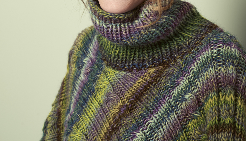 Strickanleitung Poncho aus Rigato: Bunter Poncho mit Rollkragen in Grün- und Lilatönen, gestrickt aus weicher Wolle.