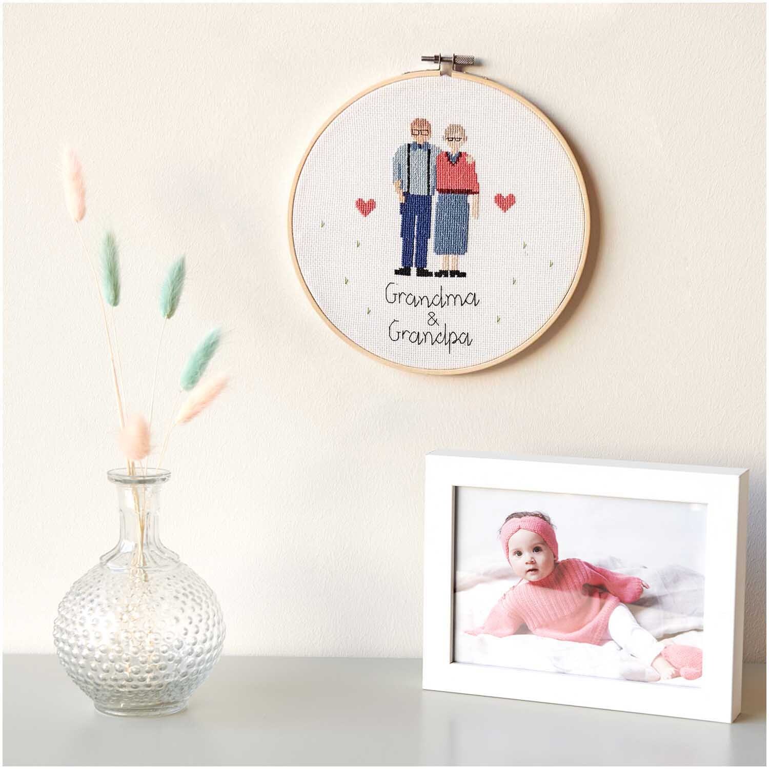 Figurico Stickpackung Grandma & Grandpa 20cm: Stickbild mit älterem Paar, Herzen, daneben Vase und Babyfoto in weißem Rahmen.