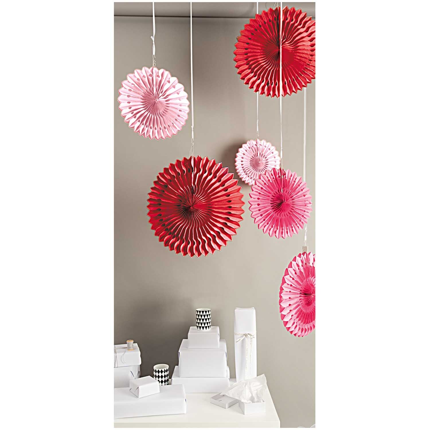 Wabenpapier Blumen rosa-rot 3 Stück von Rico Design: Hängende Dekoration in Rosa und Rot vor grauer Wand, ideal für festliche Anlässe.