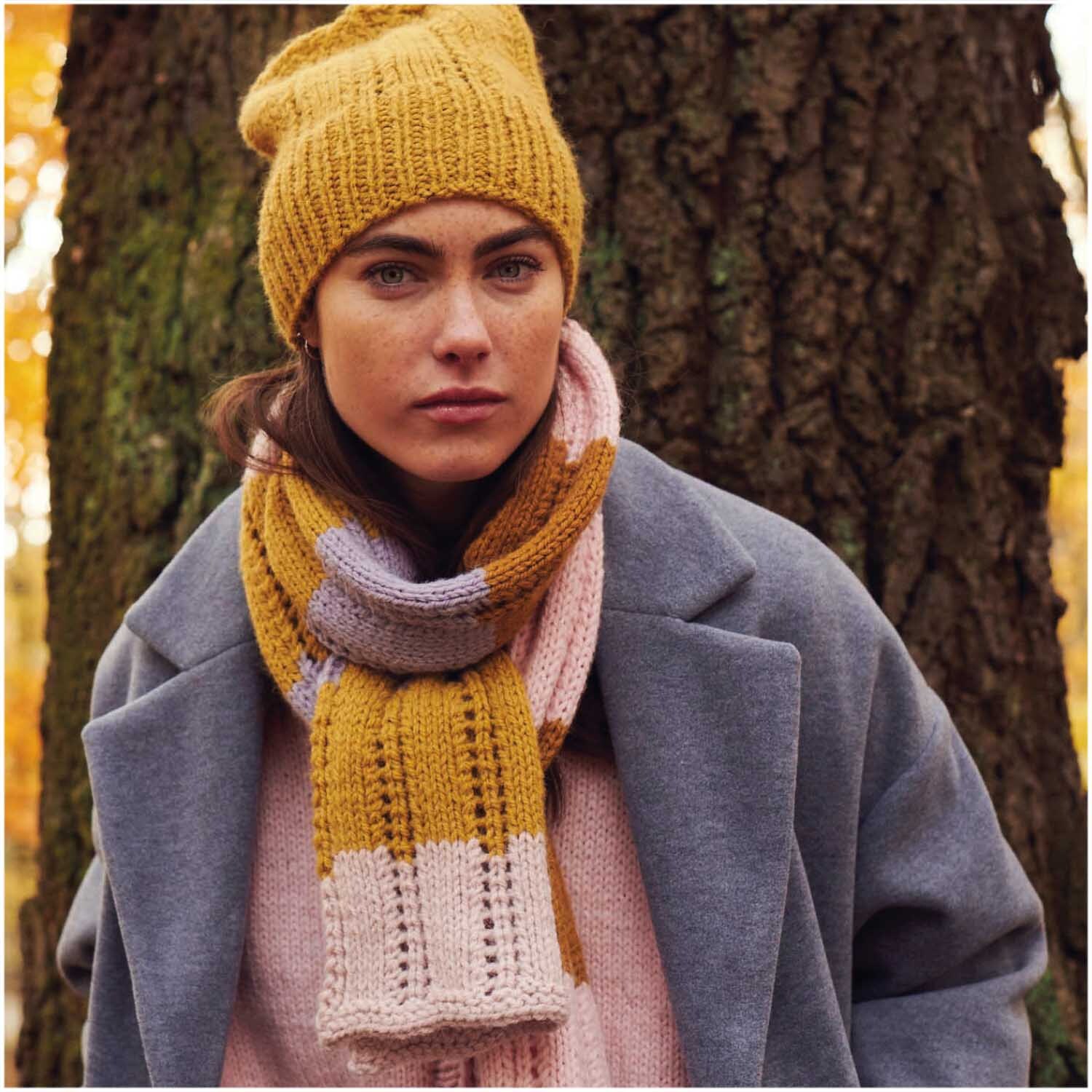 Essentials Alpaca Twist Chunky: Frau trägt gestrickte Mütze und Schal in Herbstfarben vor Baum.