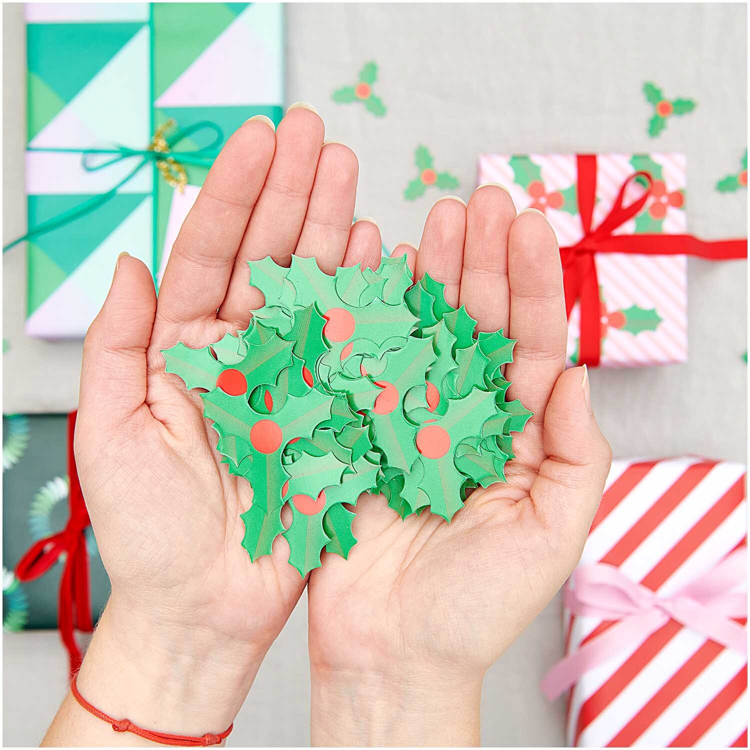 Streudeko Ilex 40g: Hände halten grüne Ilex-Blätter mit roten Beeren, umgeben von Geschenken.