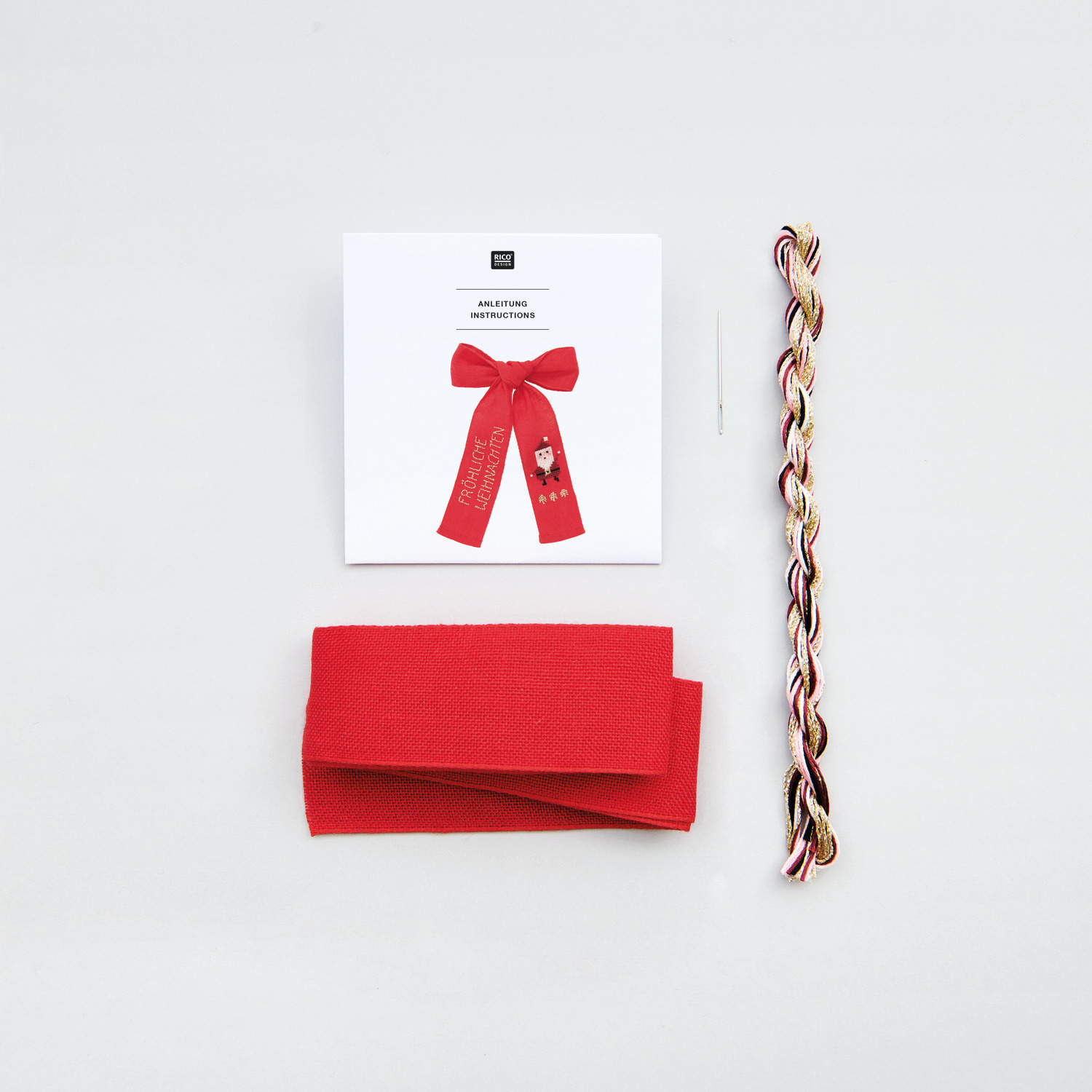 Stickpackung Schleife Nikolaus von Rico Design mit rotem Stoff, Garn und Nadel auf weißem Hintergrund.