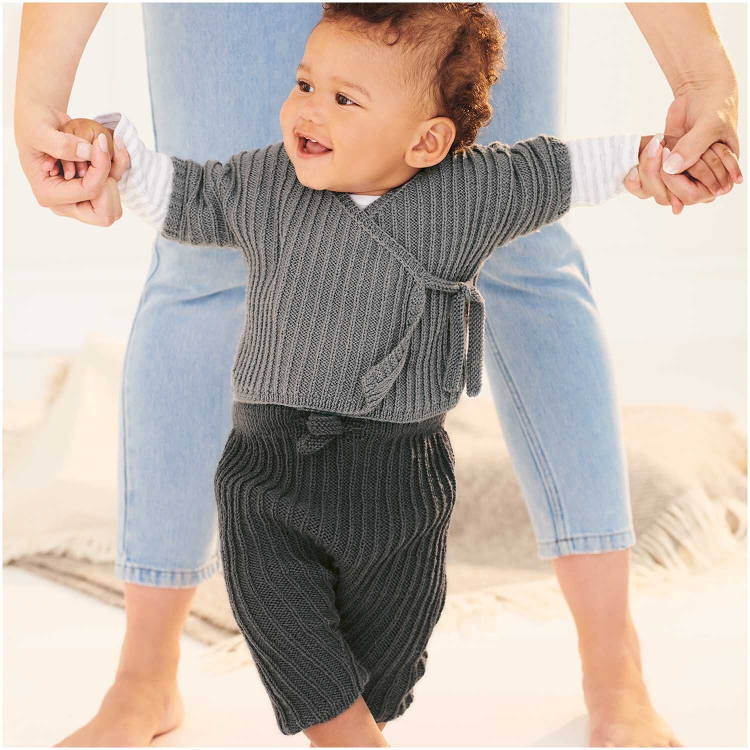 Baby Merino: Ein lächelndes Baby in anthrazitfarbener Strickkleidung von Rico Design, gehalten von einer erwachsenen Person.