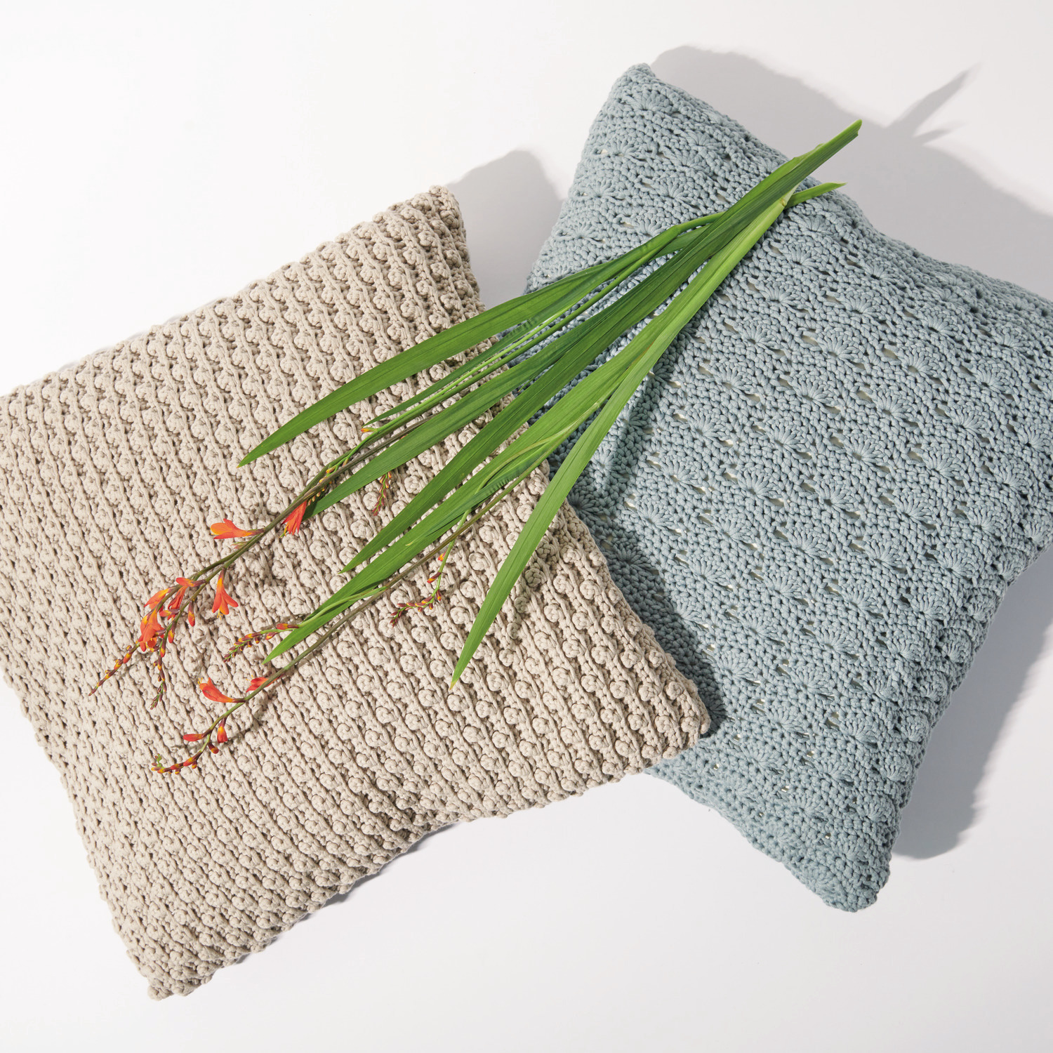 Häkelset Kissen Modell 08 aus Boho Crochet: Zwei gehäkelte Kissen in Beige und Blau mit dekorativen Blumen.