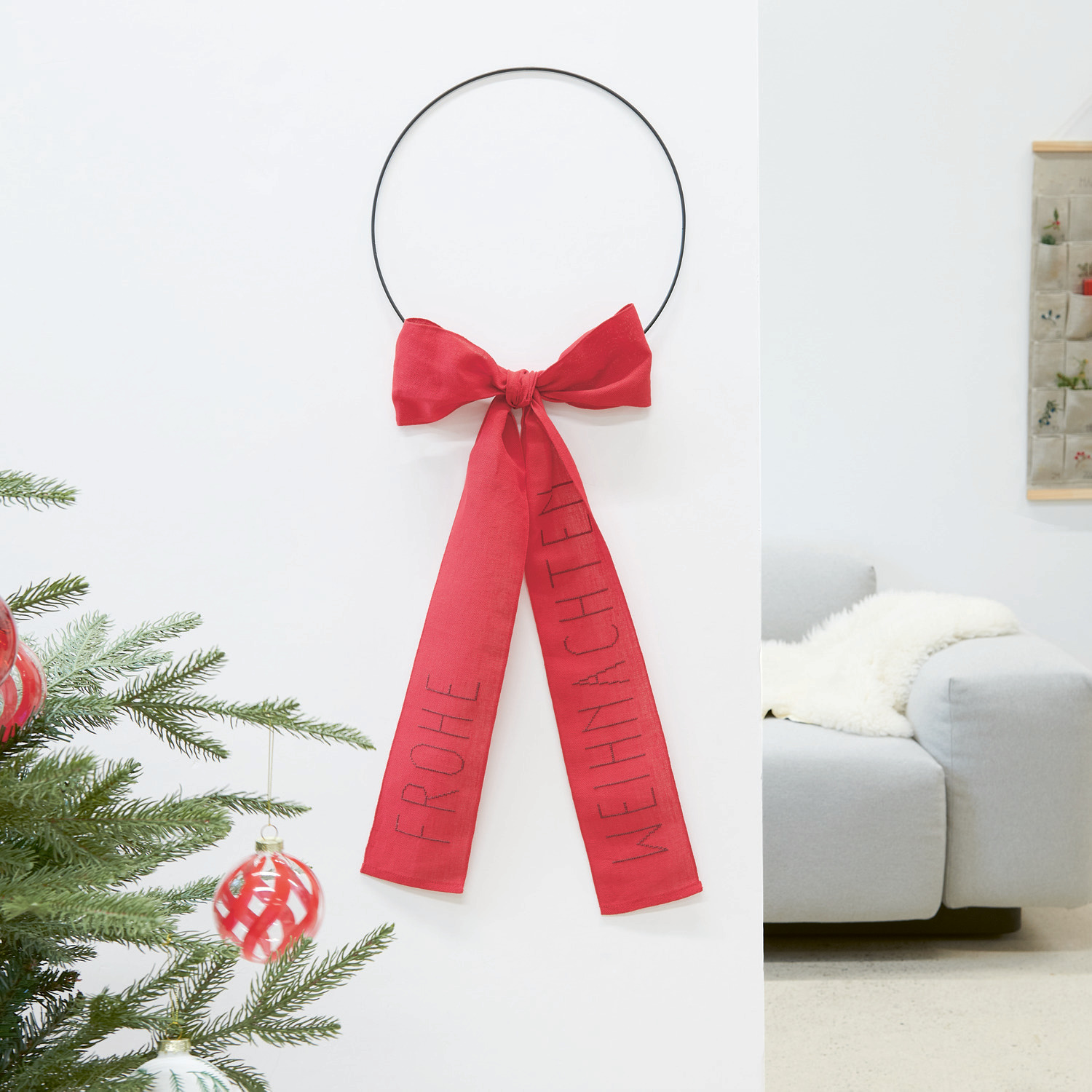 Stickpackung Schleife Frohe Weihnachten: Roter Wandkranz mit Schleife, dekoriert für festliche Stimmung. Marke: Rico Design.