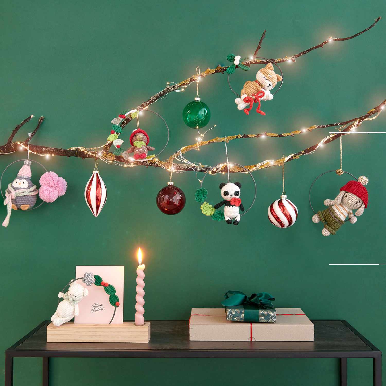 Ricorumi dk Christmas CAL Box 3: Festliche Dekoration mit gehäkelten Figuren und Kugeln an einem Ast vor grünem Hintergrund.