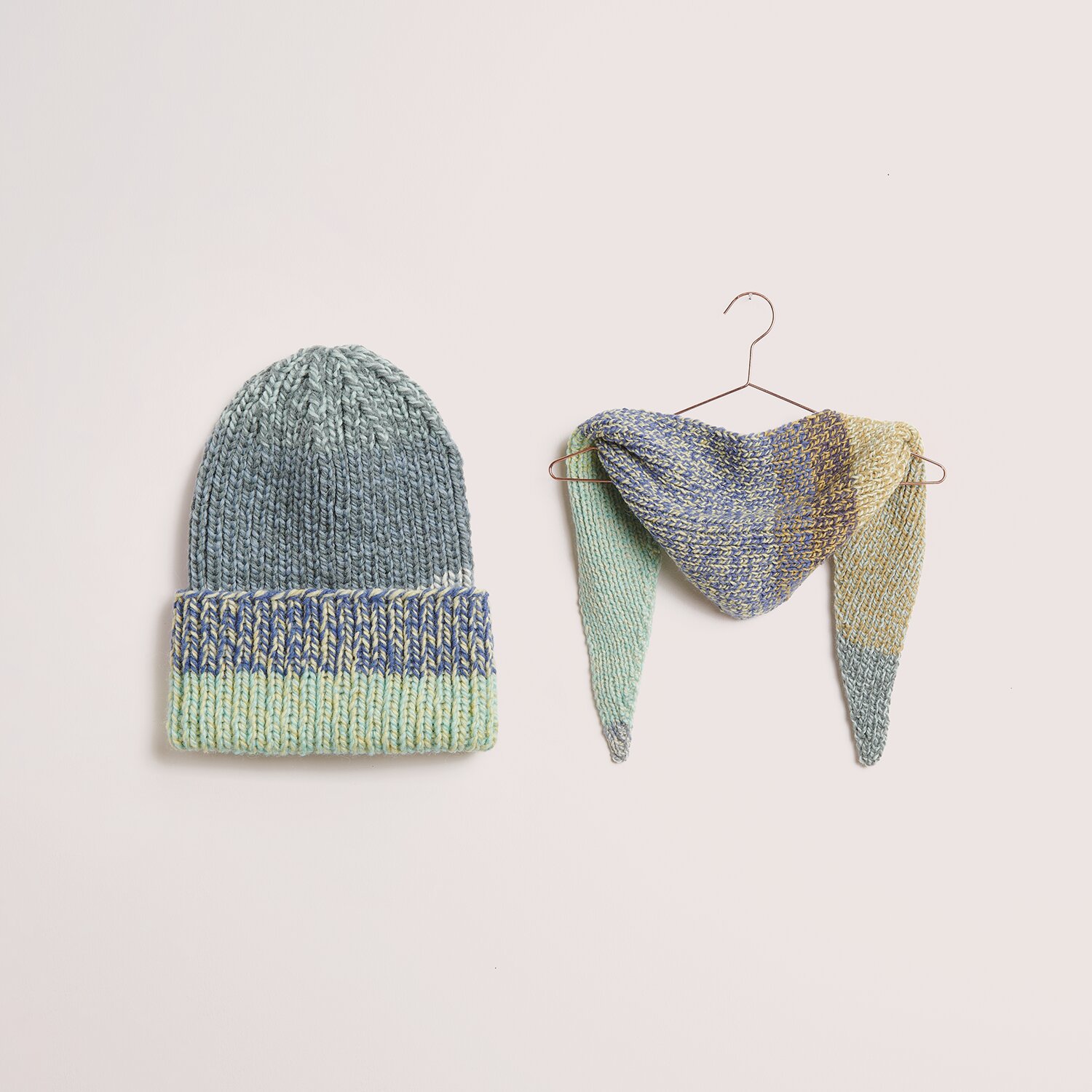 Strickset Mütze + Dreieckstuch Modell 22 aus DNM 14 in sanften Pastelltönen, präsentiert auf einem Kleiderbügel. Ideal für den Winter.