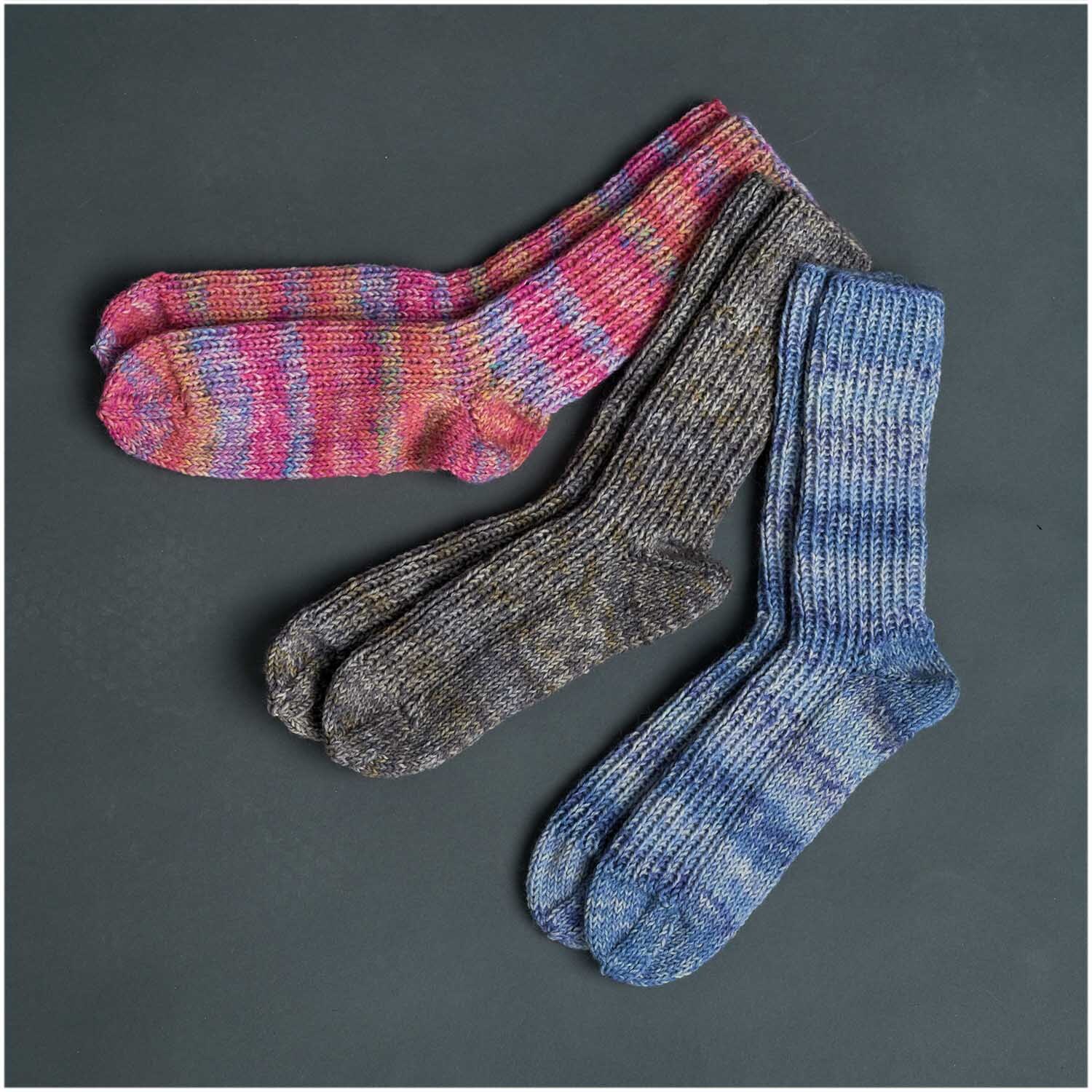 Superba Easy 8 8fädig Socken in verschiedenen Farben auf dunklem Hintergrund, gestrickt aus Rico Design Garn.