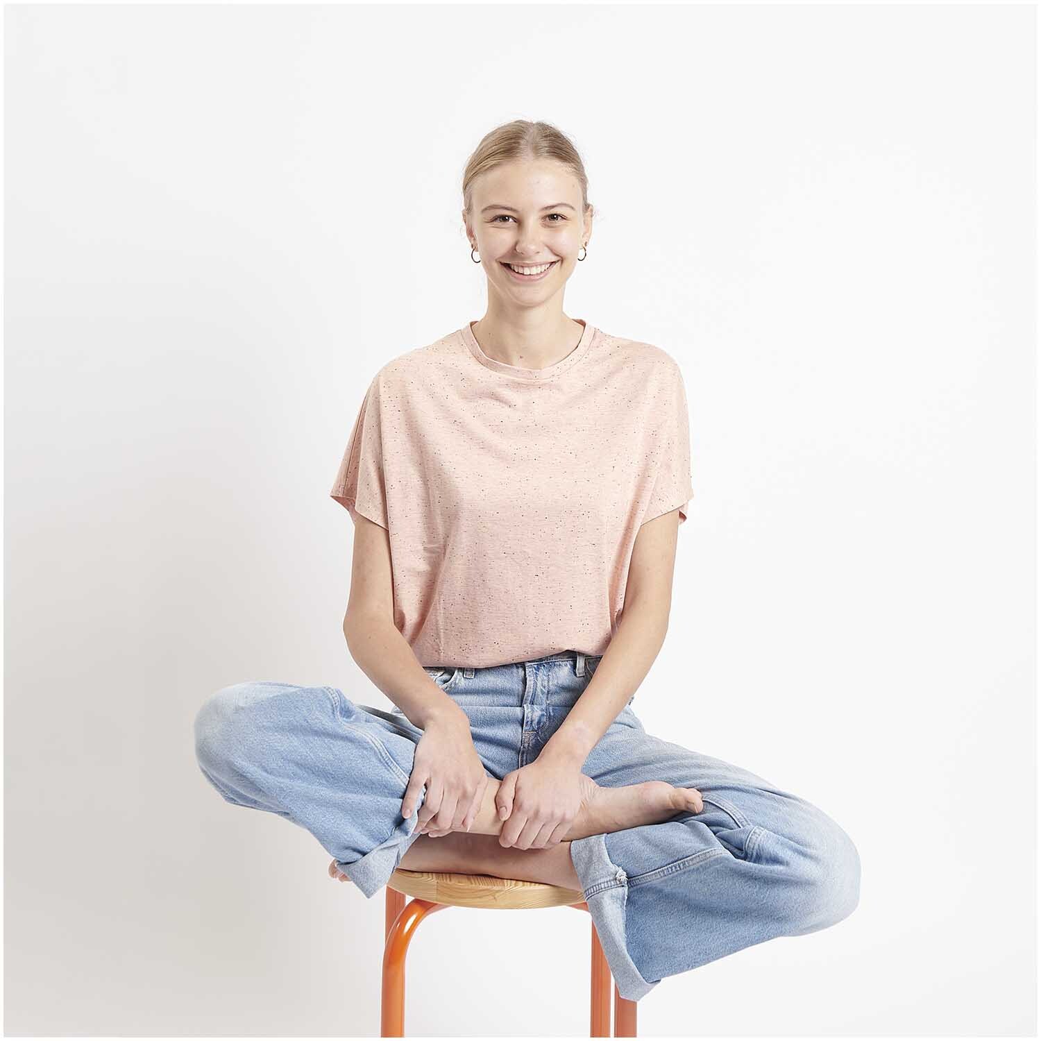 Meterware Jersey Flocken Rosa: Frau in rosa T-Shirt von Rico Design sitzt lächelnd auf einem Stuhl.