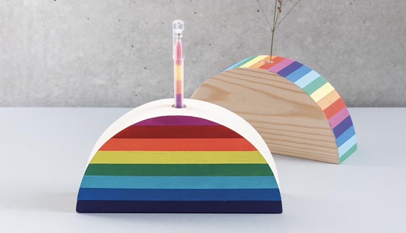 Anleitung kunterbunter Regenbogen: Zwei halbrunde Holzobjekte mit Regenbogenfarben, eines mit Vase.