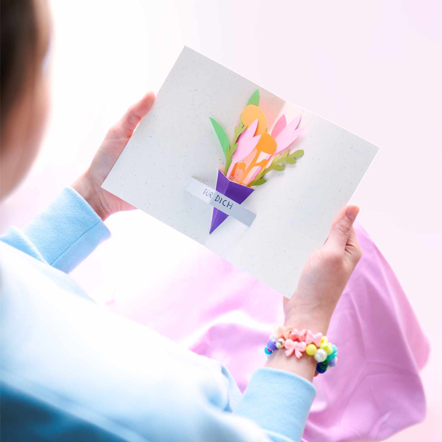 Bastelanleitung Pop Up Karte: Person hält eine Karte mit buntem Blumenstrauß-Design in den Händen.