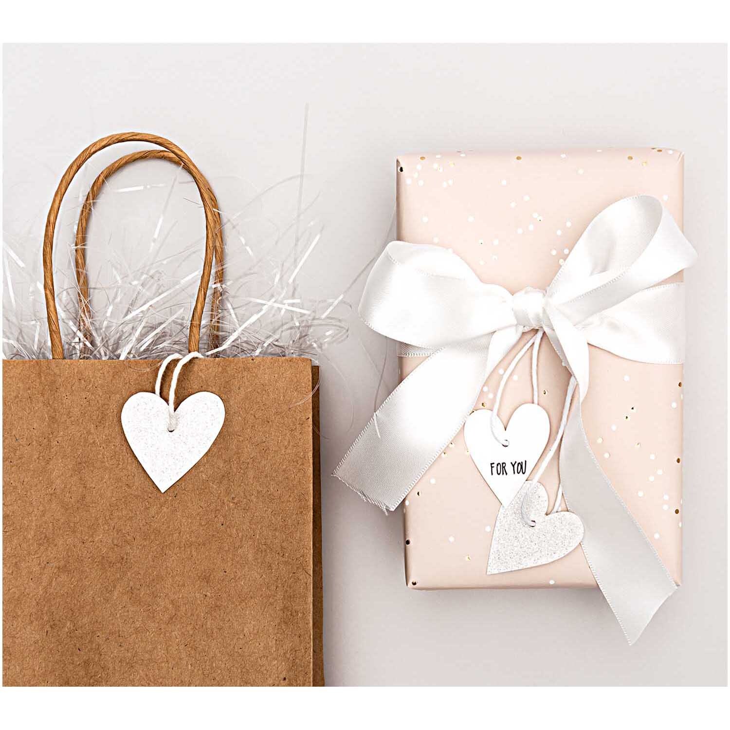 Paper Poetry Papieranhänger Herzen in Glitter-Optik schmücken ein Geschenk und eine Papiertüte. Ideal für kreative Verpackungen.