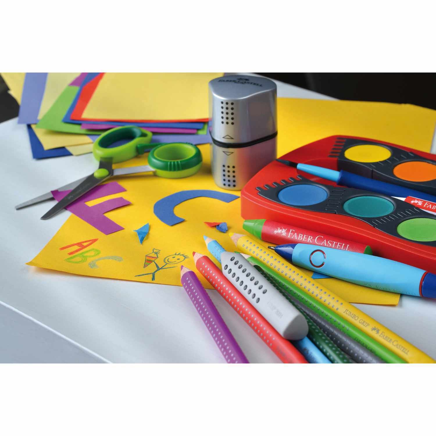 Farbkasten Connector 24 Farben von Faber Castell, umgeben von bunten Stiften, Schere und Papier.