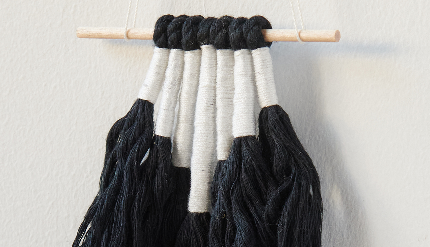 Bastelanleitung stylisher Wandbehang: Handgefertigter Makramee-Wandbehang in Schwarz-Weiß an Holzstab.