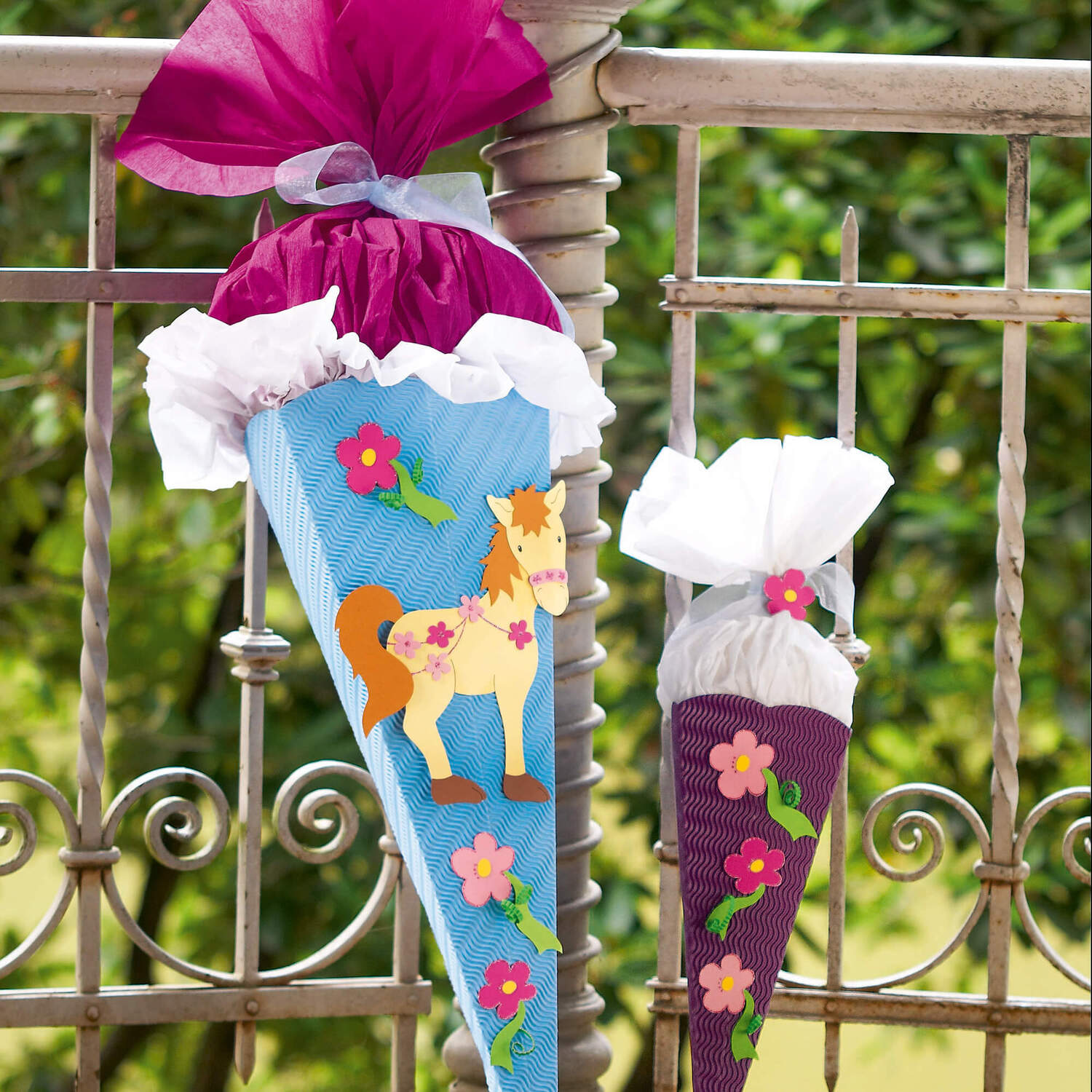 Bastelanleitung Pony-Schultüte: Zwei bunte Schultüten mit Pony- und Blumenmotiven an einem Zaun.