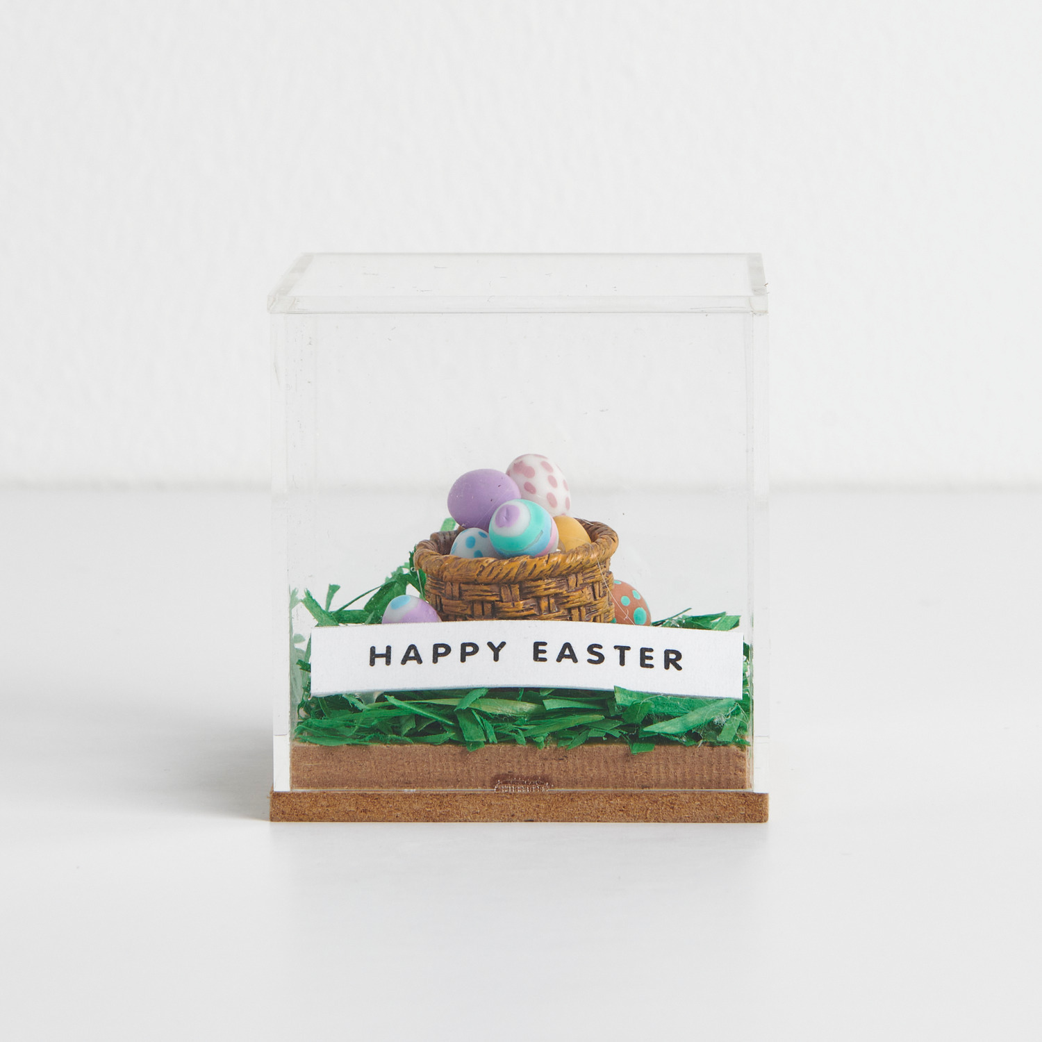 Miniatur Eierkorb mit 8 Eiern in einer Figurico Dekohaube Würfel. Bunte Eier auf grünem Gras.