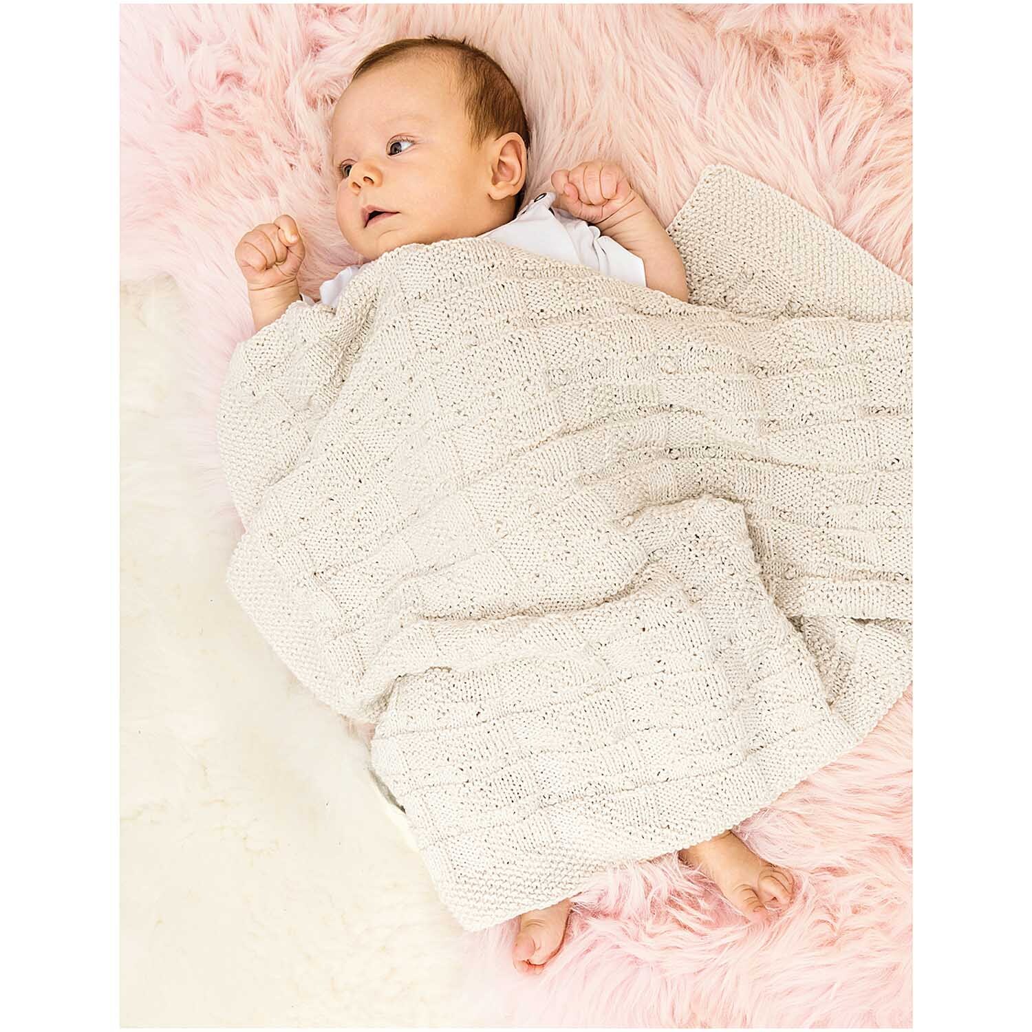 Rico Baby Cotton Soft dk: Ein Baby liegt auf einer rosa Decke, eingewickelt in ein weiches, gestricktes Tuch.