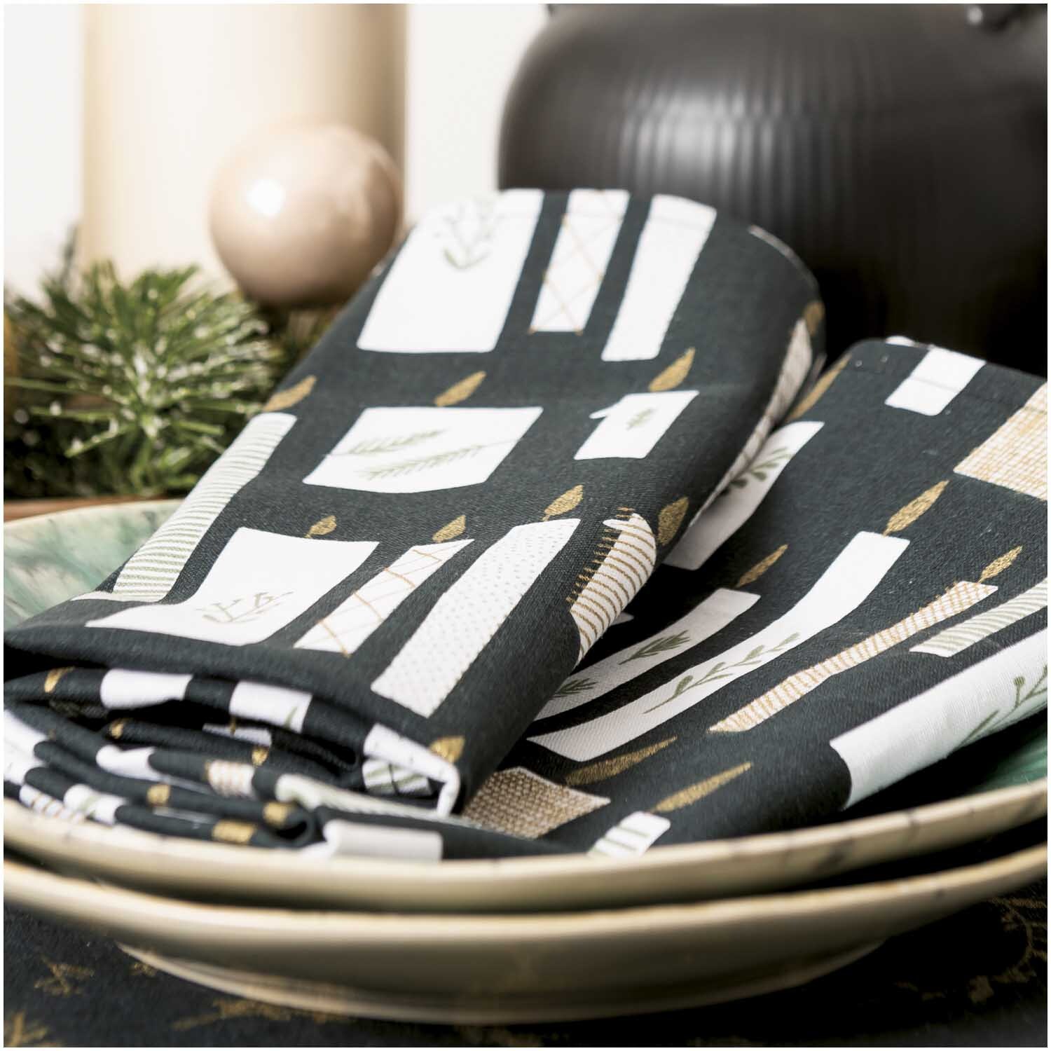 Druckstoff Nostalgic Christmas Kerzen in Schwarz-Gold von Rico Design, dekoriert mit Kerzenmotiv auf einem Tisch mit Tannenzweigen.