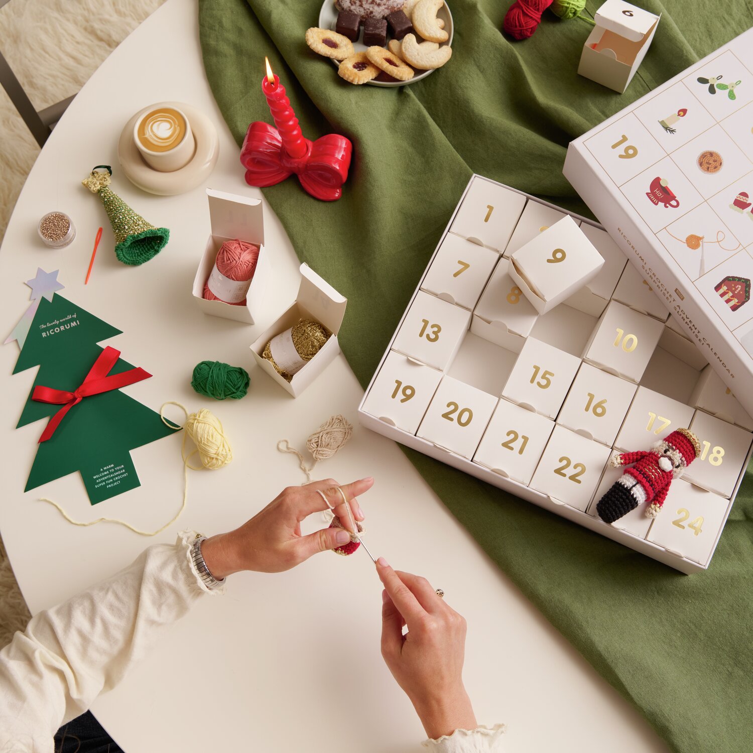 Ricorumi Adventskalender Weihnachtsmarkt von Rico Design auf einem Tisch mit Bastelmaterialien und weihnachtlicher Dekoration.