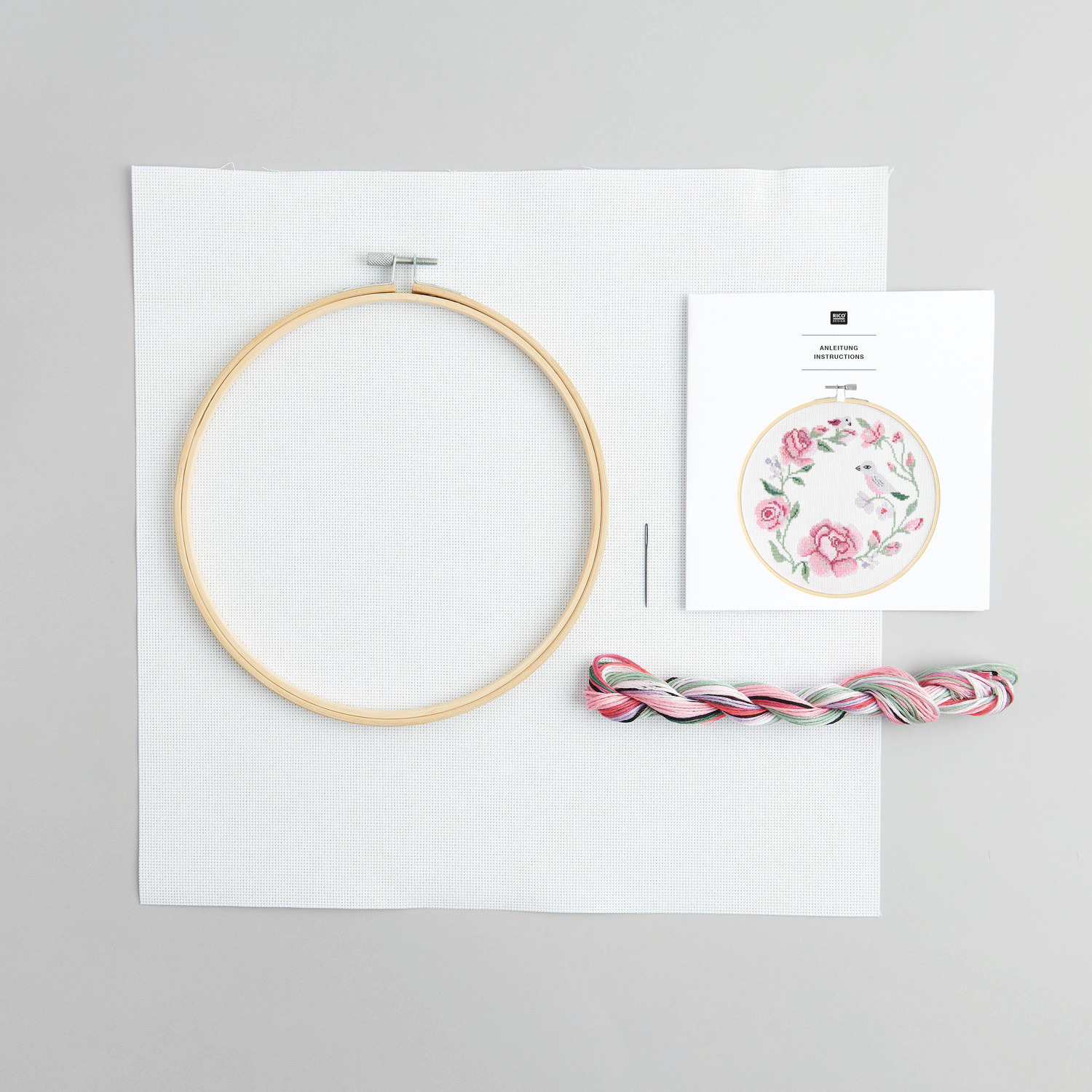 Stickpackung Kranz aus Rosen von Rico Design zeigt einen Stickrahmen, Garn und Anleitung auf grauem Hintergrund. Ideal für kreative Handarbeiten.
