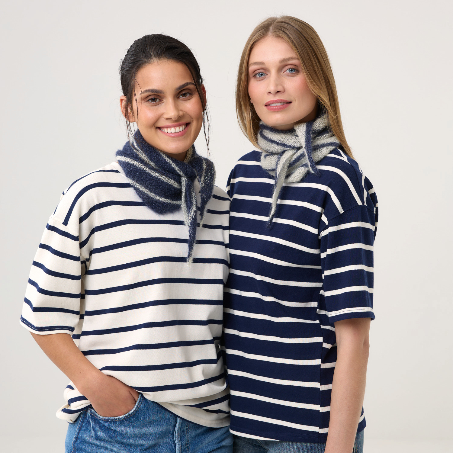 Strickset Dreieckstuch Modell 22: Zwei Frauen tragen gestreifte Shirts und gestrickte Tücher in Blau und Grau. Ideal für modische Akzente.