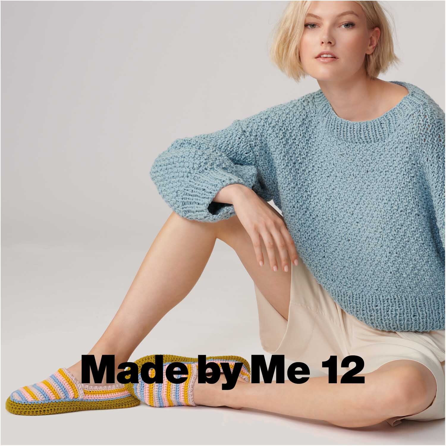Essentials Organic Cotton aran: Frau in blauem Strickpullover und gestreiften Hausschuhen.
