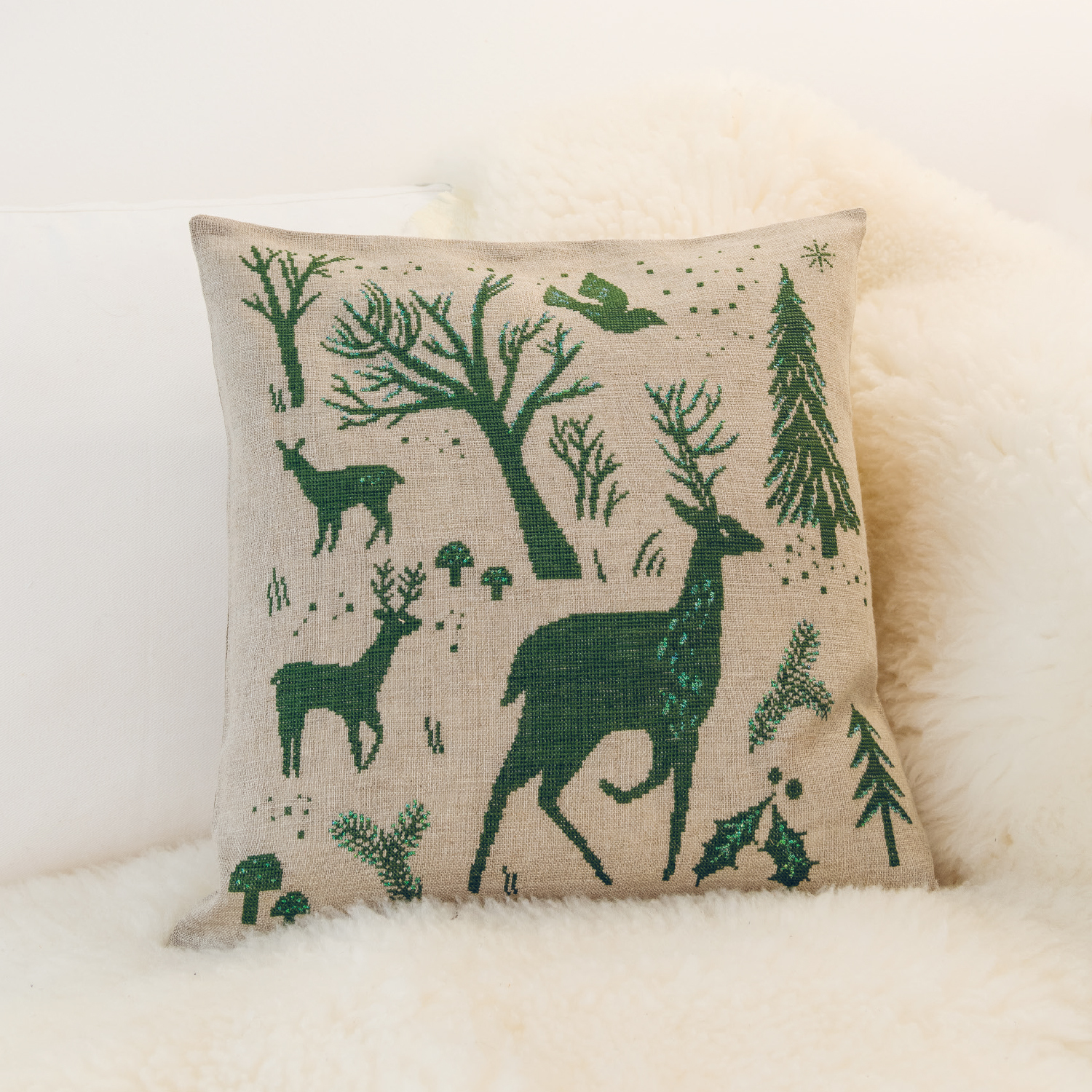 Stickanleitung Weihnachtliches Kissen gestalten: Kissen mit grünen Waldmotiven und Rentieren auf beigem Stoff, ideal für festliche Dekoration.