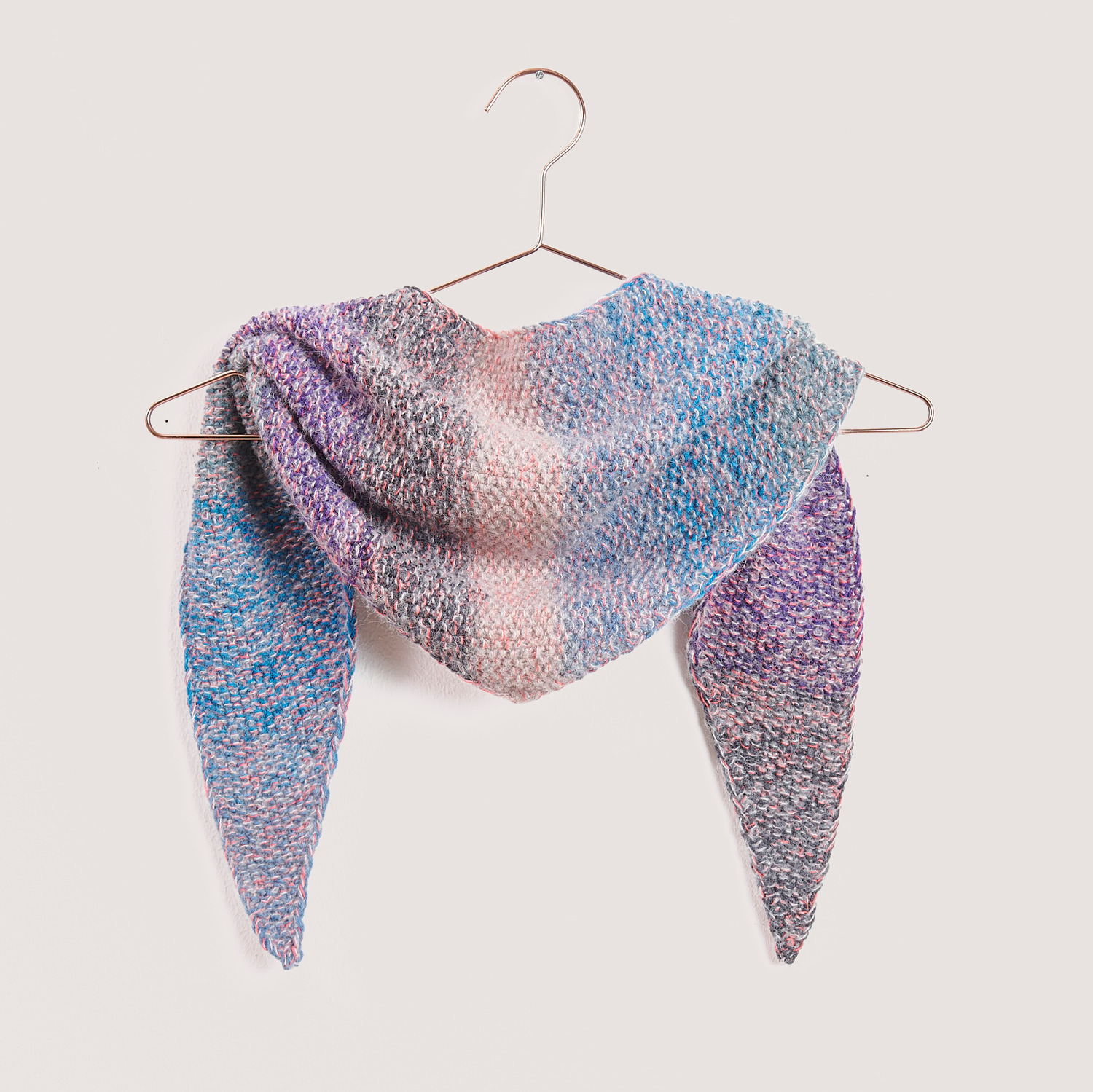Strickset Mini Dreieckstuch Modell 01b in sanften Pastelltönen, aufgehängt an einem Kleiderbügel. Ideal für stilvolle Handarbeitsprojekte.