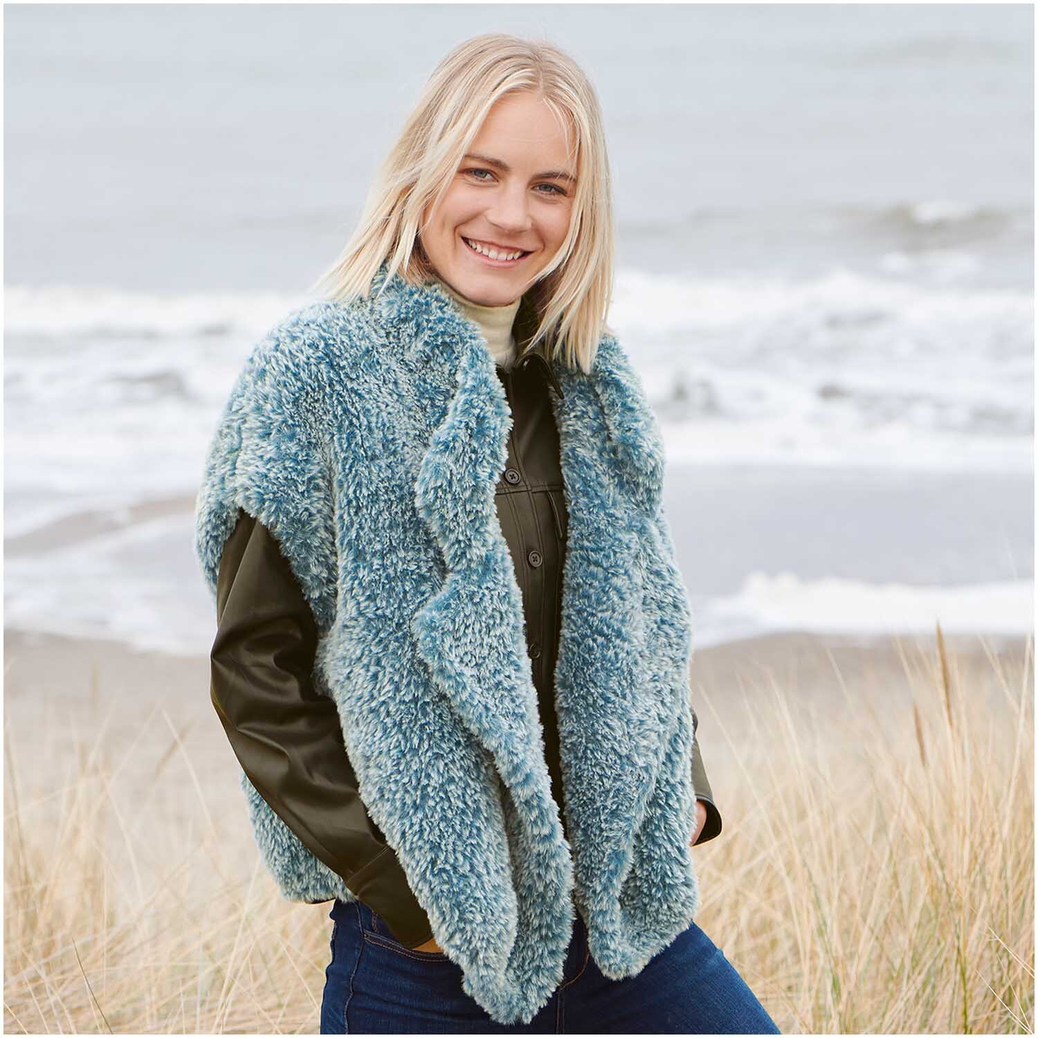 Creative Petit Lapin Super Chunky: Frau am Strand in flauschiger, blau-grauer Weste von Rico Design.
