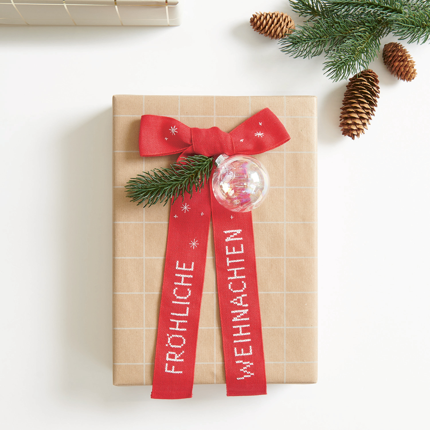 Stickbuch Put a Bow on It Nr. 185: Geschenk mit roter Schleife und Tannenzweig, verziert mit "Fröhliche Weihnachten".