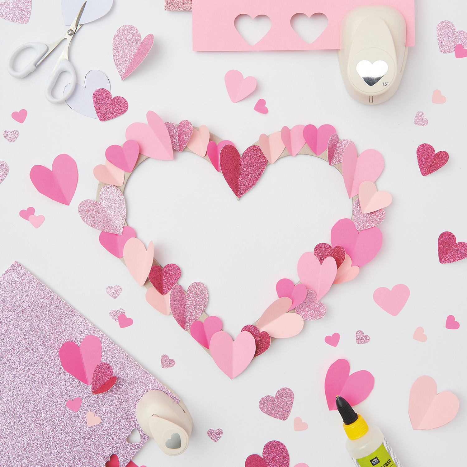 Bastelanleitung 3D-Herz zum Muttertag: Herz aus rosa und roten Papierherzen, umgeben von Bastelmaterialien.