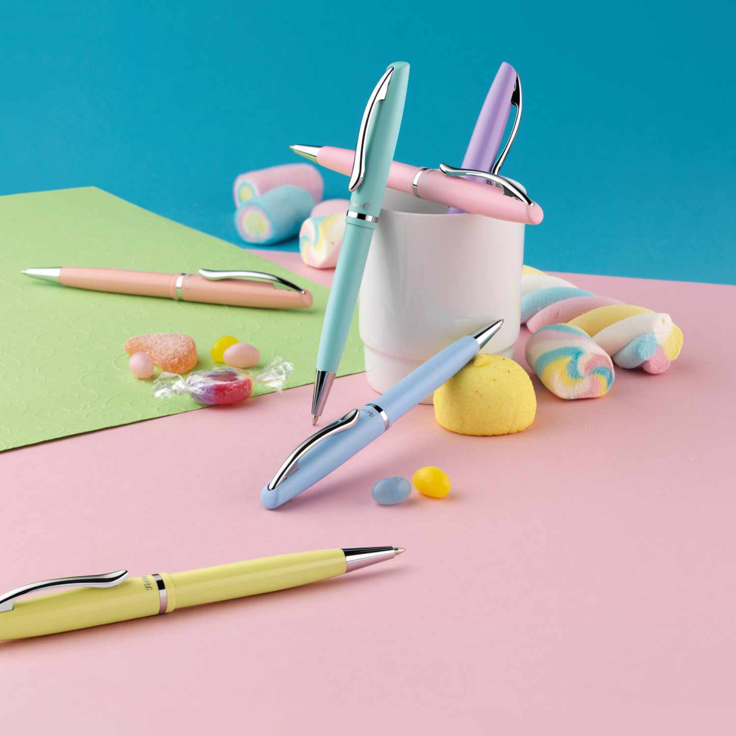 Kugelschreiber Jazz Pastell K36 von Pelikan in verschiedenen Pastellfarben auf buntem Hintergrund mit Süßigkeiten und Notizpapier.
