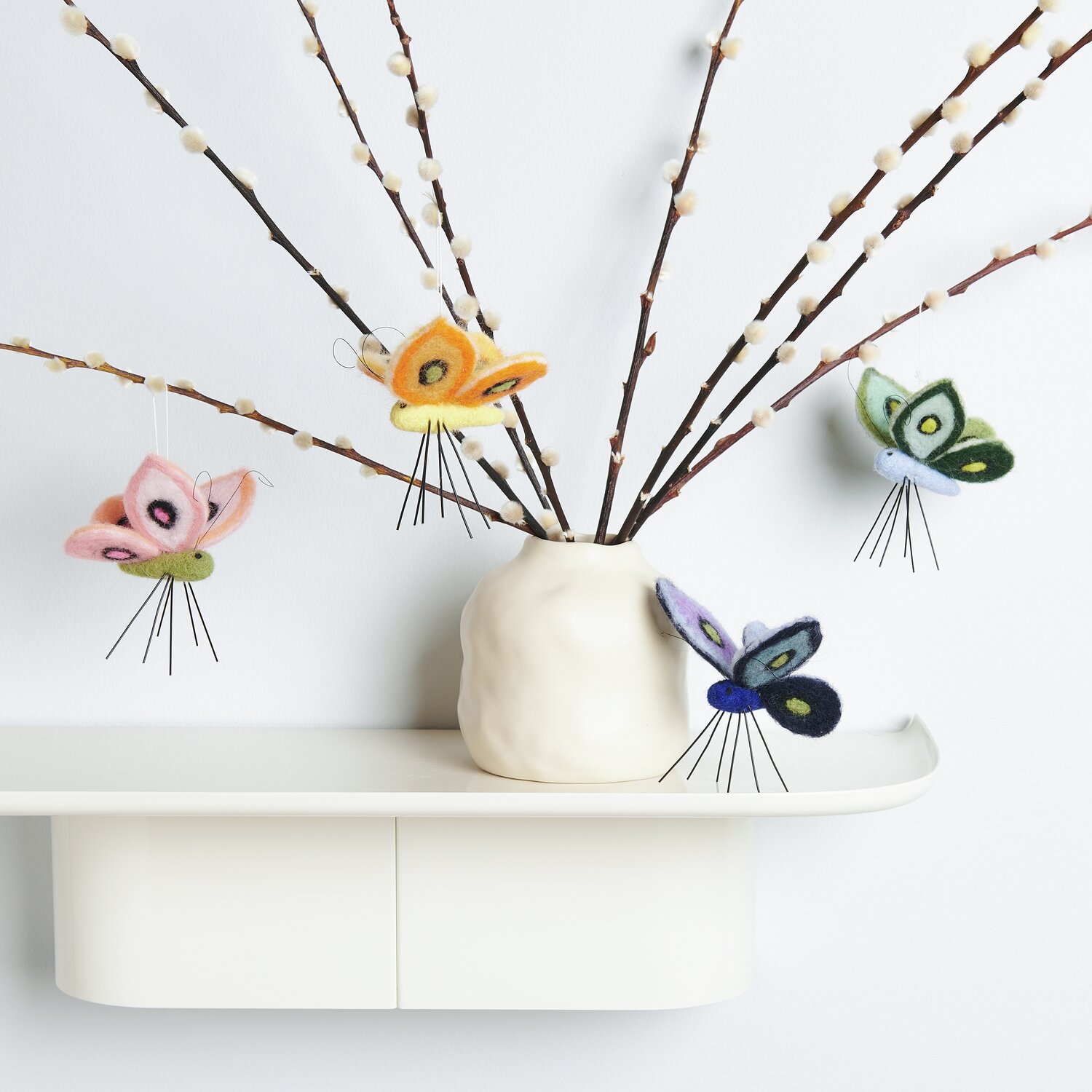 Aufhänger Filz-Schmetterling: Bunte Filz-Schmetterlinge von Rico Design an Zweigen in weißer Vase.
