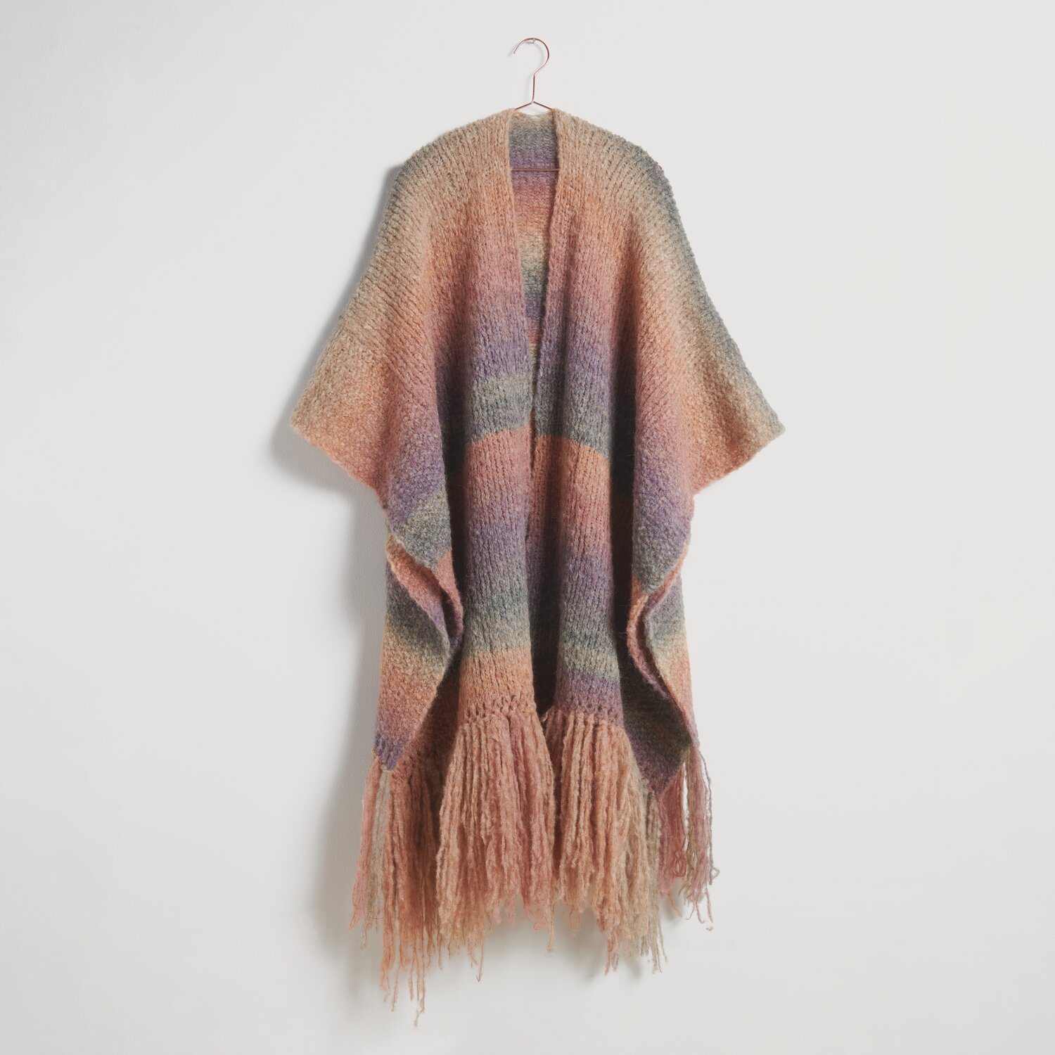 Strickset Poncho Modell 07b aus Die Neue Masche No. 10, mehrfarbig mit Fransen, hängt an einem Haken. Ideal für stilvolle, warme Outfits.