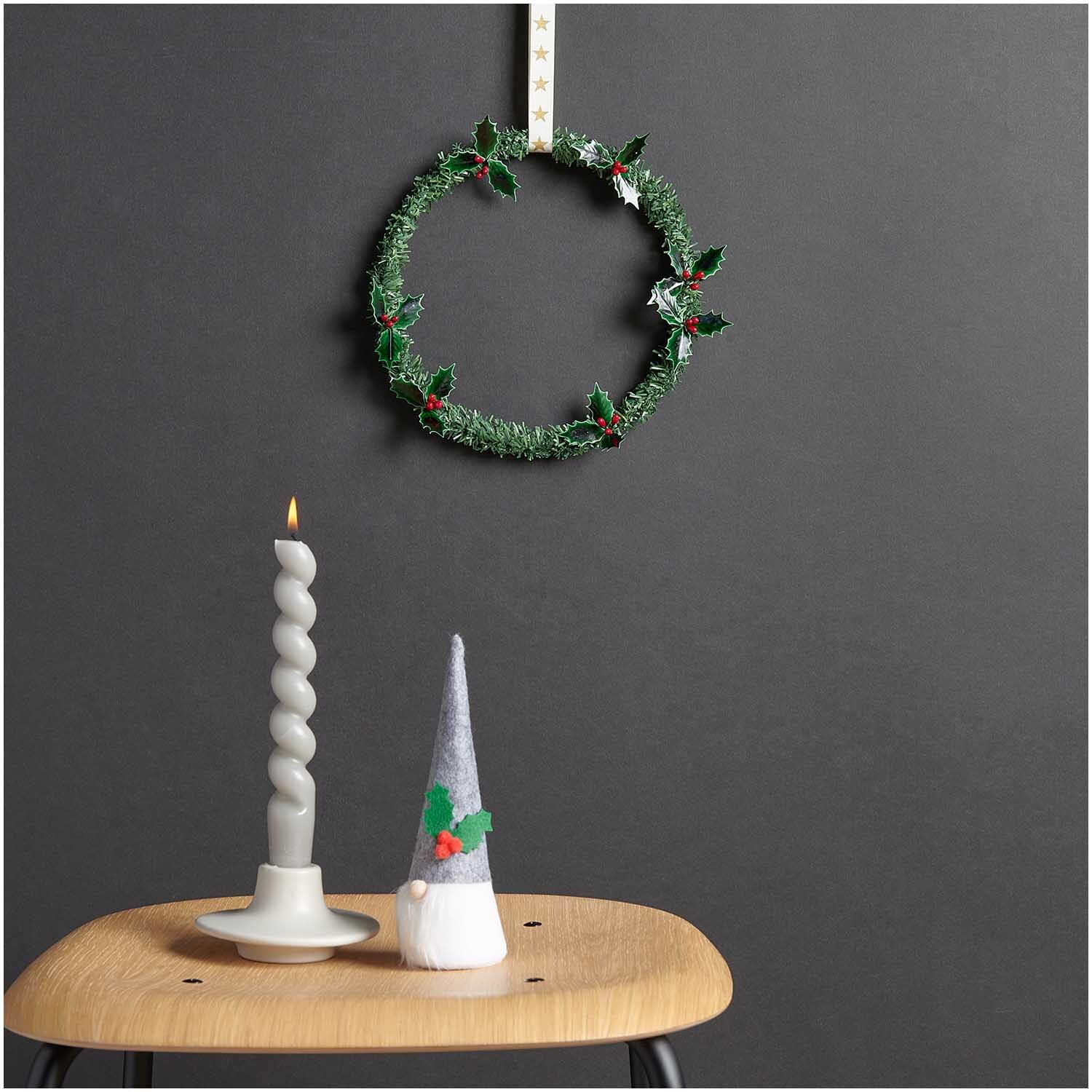 Tannengirlande grün Ø 2cm 2,5m von Rico Design an einer Wand, daneben eine Kerze und ein Deko-Zwerg auf einem Holzstuhl.