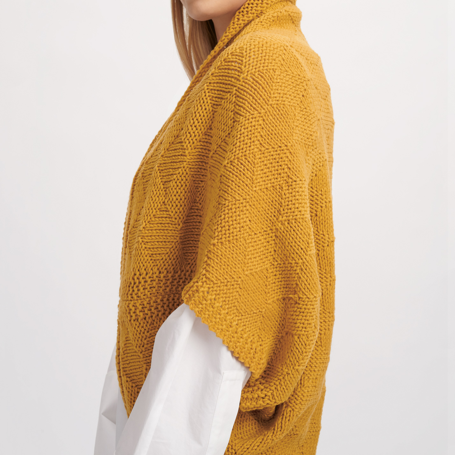 Strickanleitung Poncho aus Classik: Frau trägt gelben Strickponcho über weißem Hemd, seitliche Ansicht.