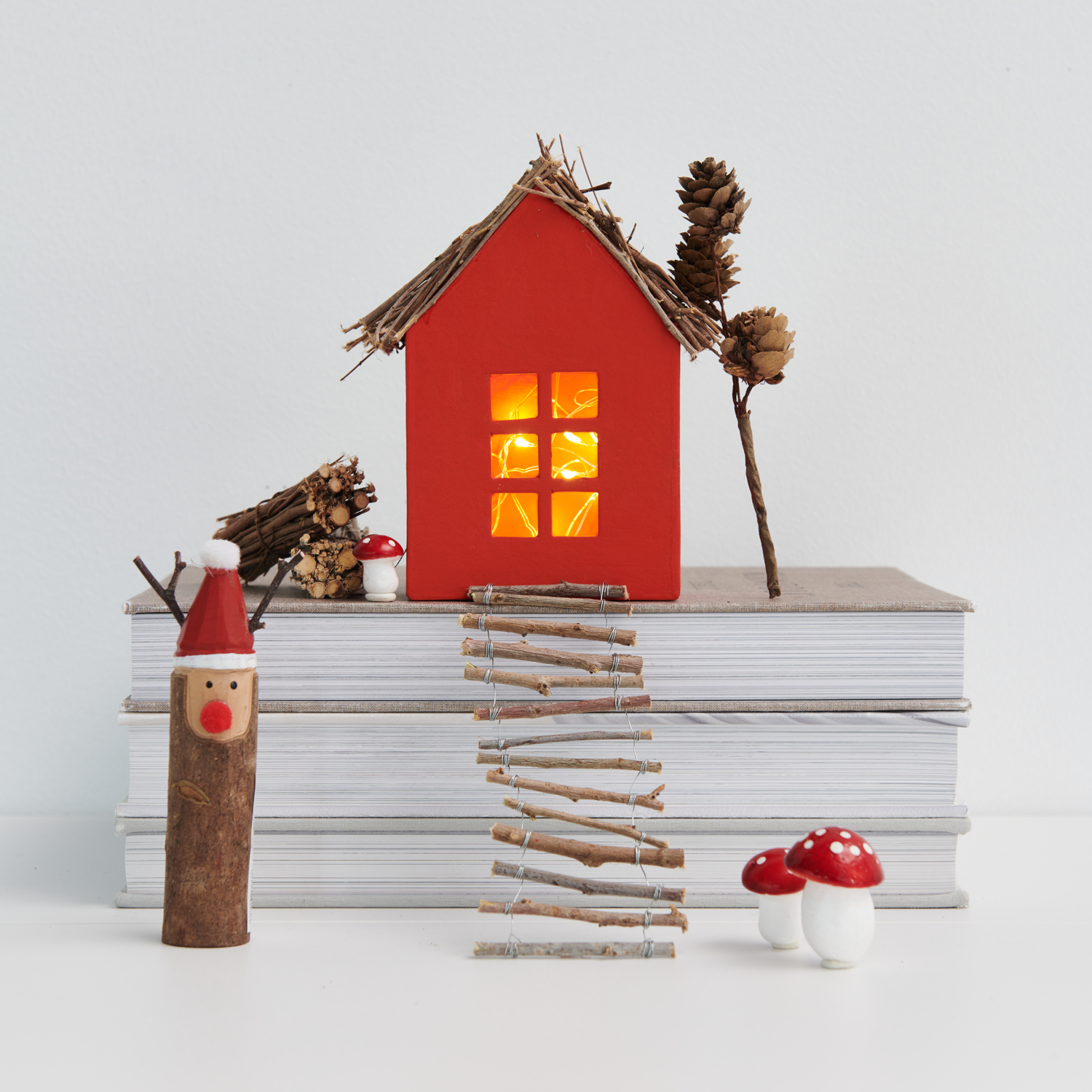 Bastelanleitung Wichtelhaus aus Pappmaché: Rotes Haus mit Zweigen, Pilzen und Wichtel auf Büchern.
