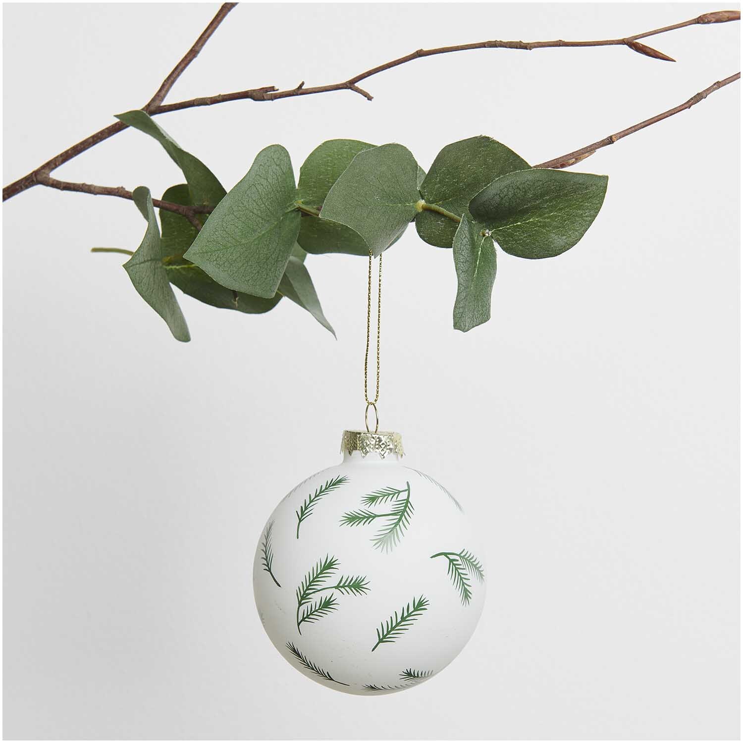 Glaskugel Baumschmuck mit Tannenzweigen hängt an einem Ast, verziert mit grünen Zweigen.