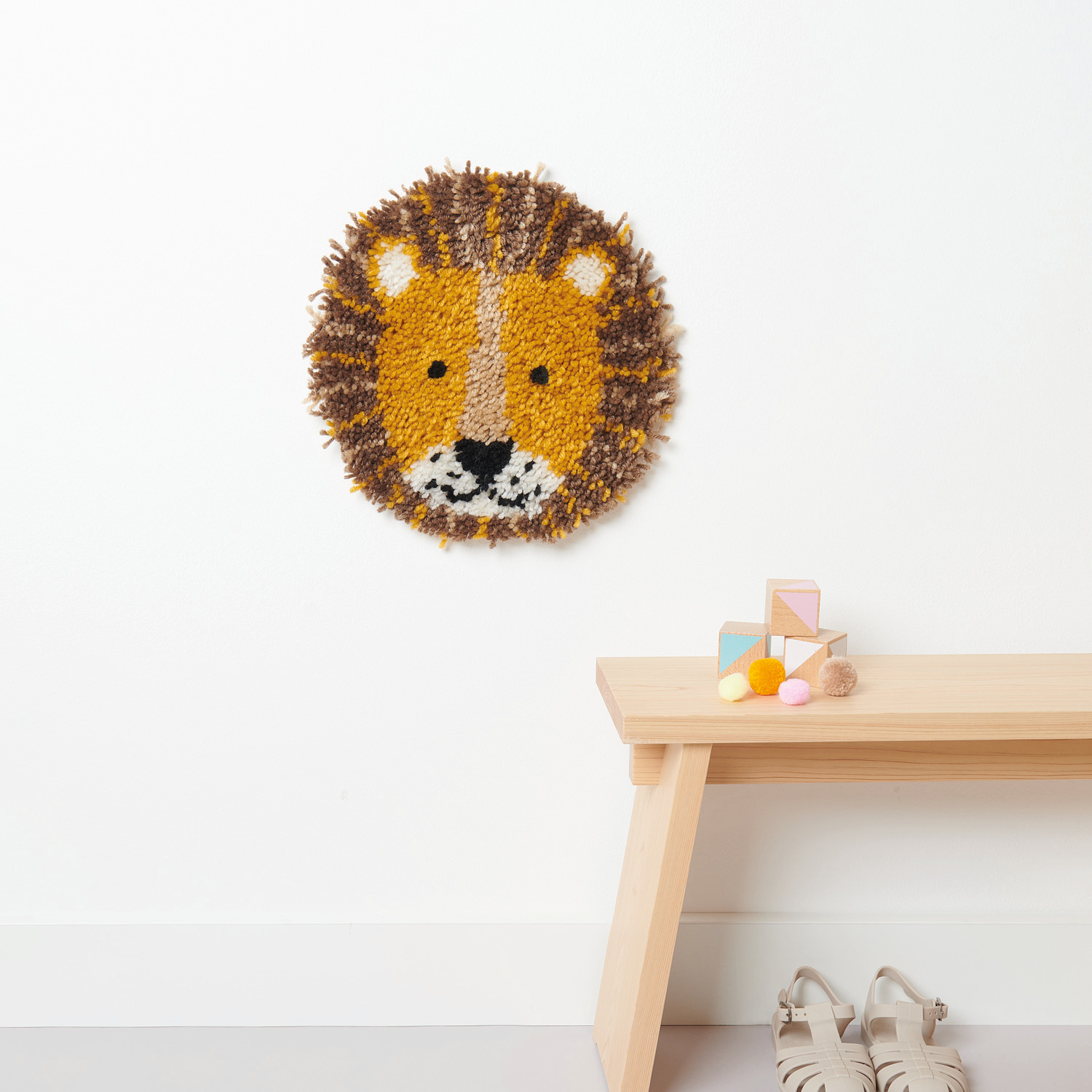 Rico Hooki Hooki Knüpfset Wandbehang Löwe zeigt einen runden Löwenkopf an einer weißen Wand.