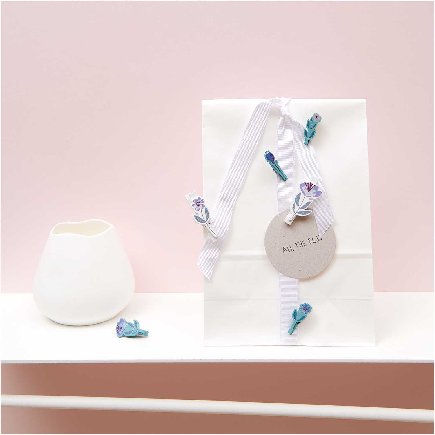 Dekoklammern Blume 8 Stück in Grün-Blau von Rico Design, dekorativ an einer weißen Geschenkverpackung befestigt.