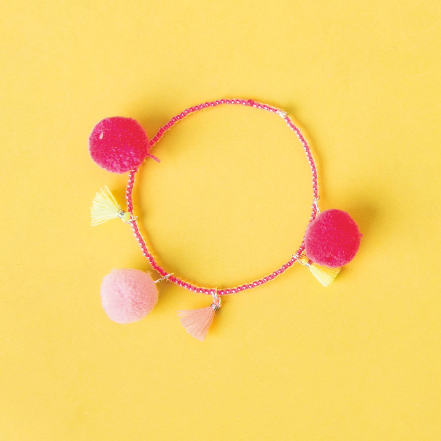 Bastelanleitung Perlenarmband mit Quasten und Pompons auf gelbem Hintergrund, farbenfroh gestaltet.