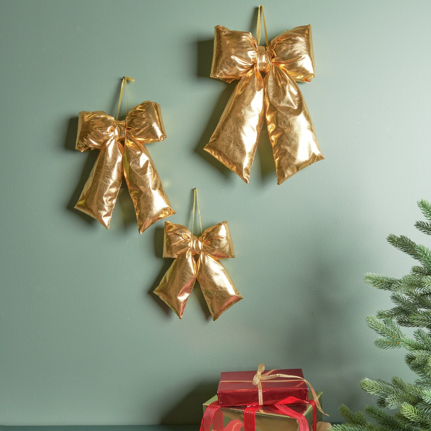 Weihnachtsschleife Gold: Drei glänzende Schleifen von Rico Design an grüner Wand, festlich dekoriert.